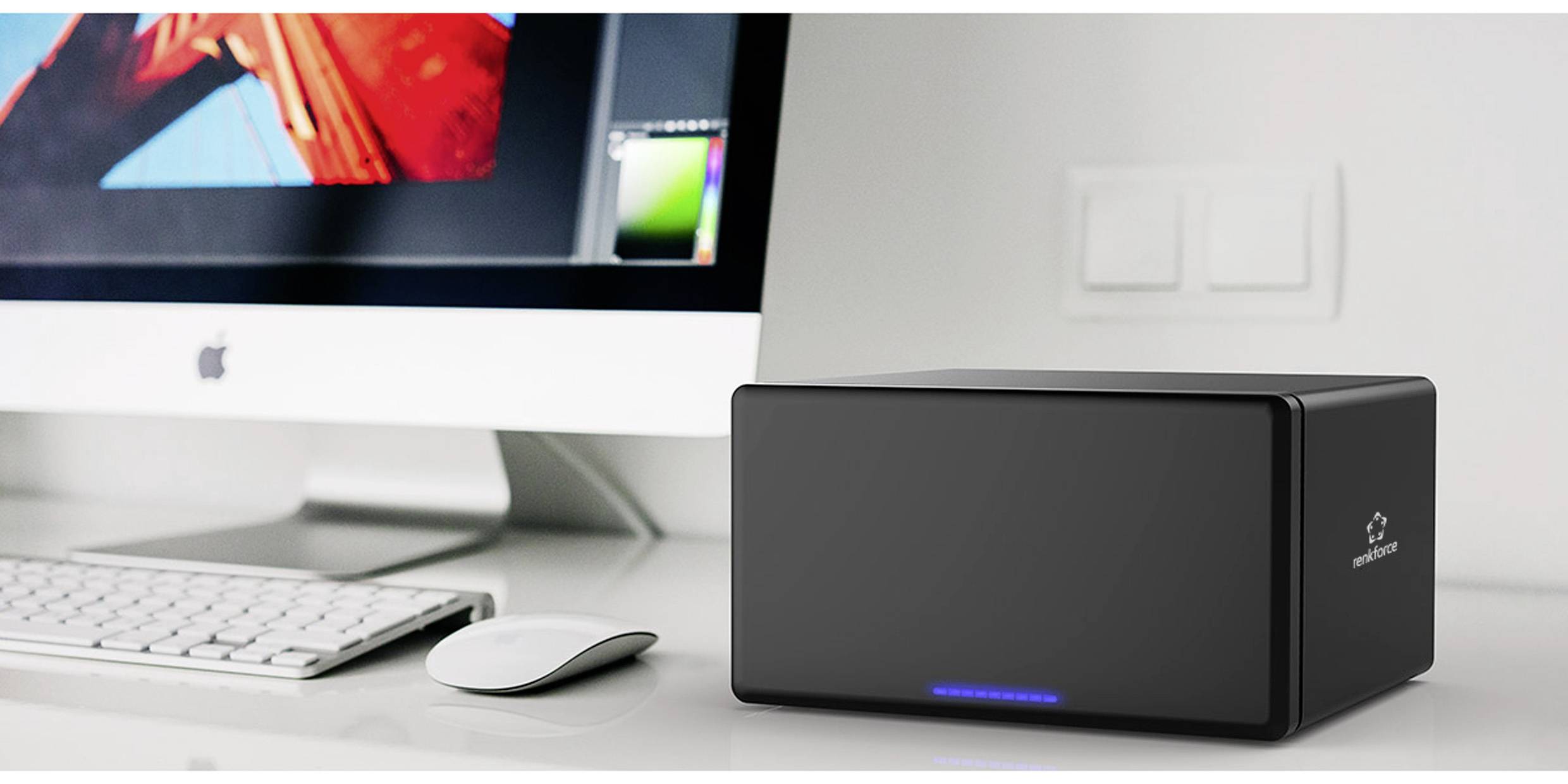 Czarny外置硬盘盒，带蓝色LED指示灯，放置在桌子上，位于键盘和显示器旁边。