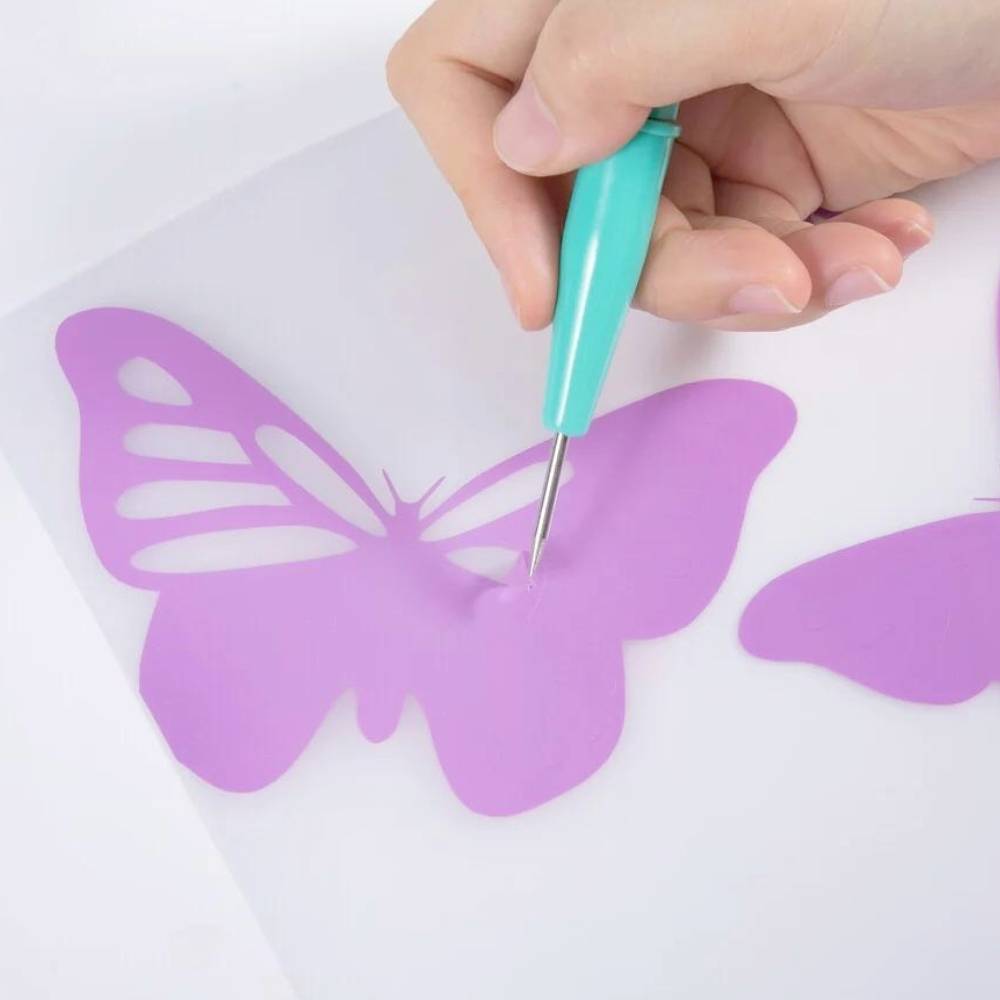 Dłoń używa zielonego narzędzia do wycinania motyla z fioletowego papieru.