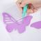 Dłoń używa zielonego narzędzia do wycinania motyla z fioletowego papieru.