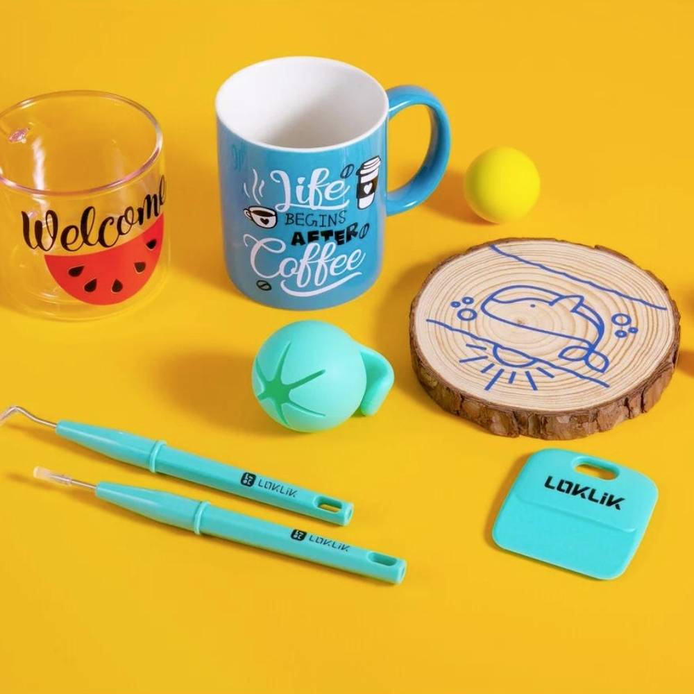 Różne kolorowe przybory kuchenne na żółtym tle: kubki, szklanka, podkładka drewniana, piłeczka do ping-ponga, niebieskie długopisy.