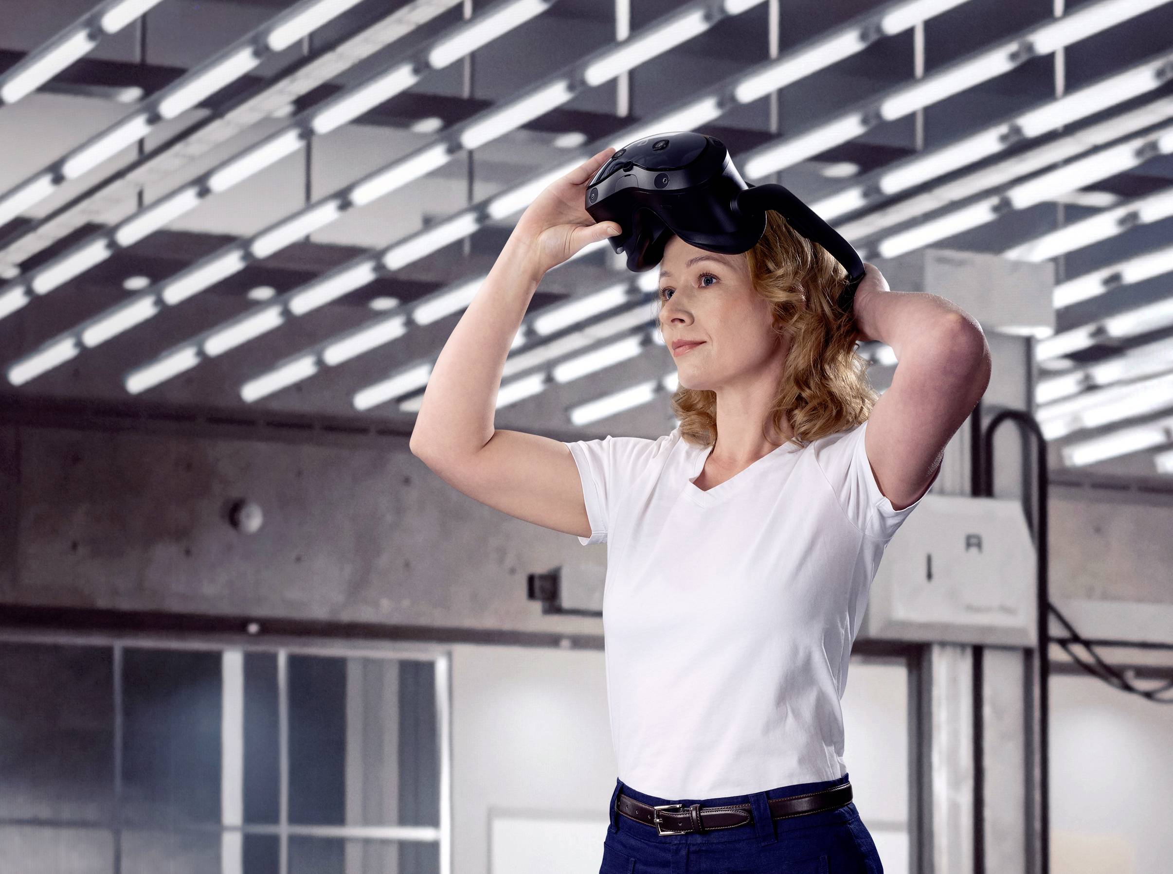 Osoba zakłada gogle VR w nowoczesnym, futurystycznym pomieszczeniu z wieloma światłami na suficie.