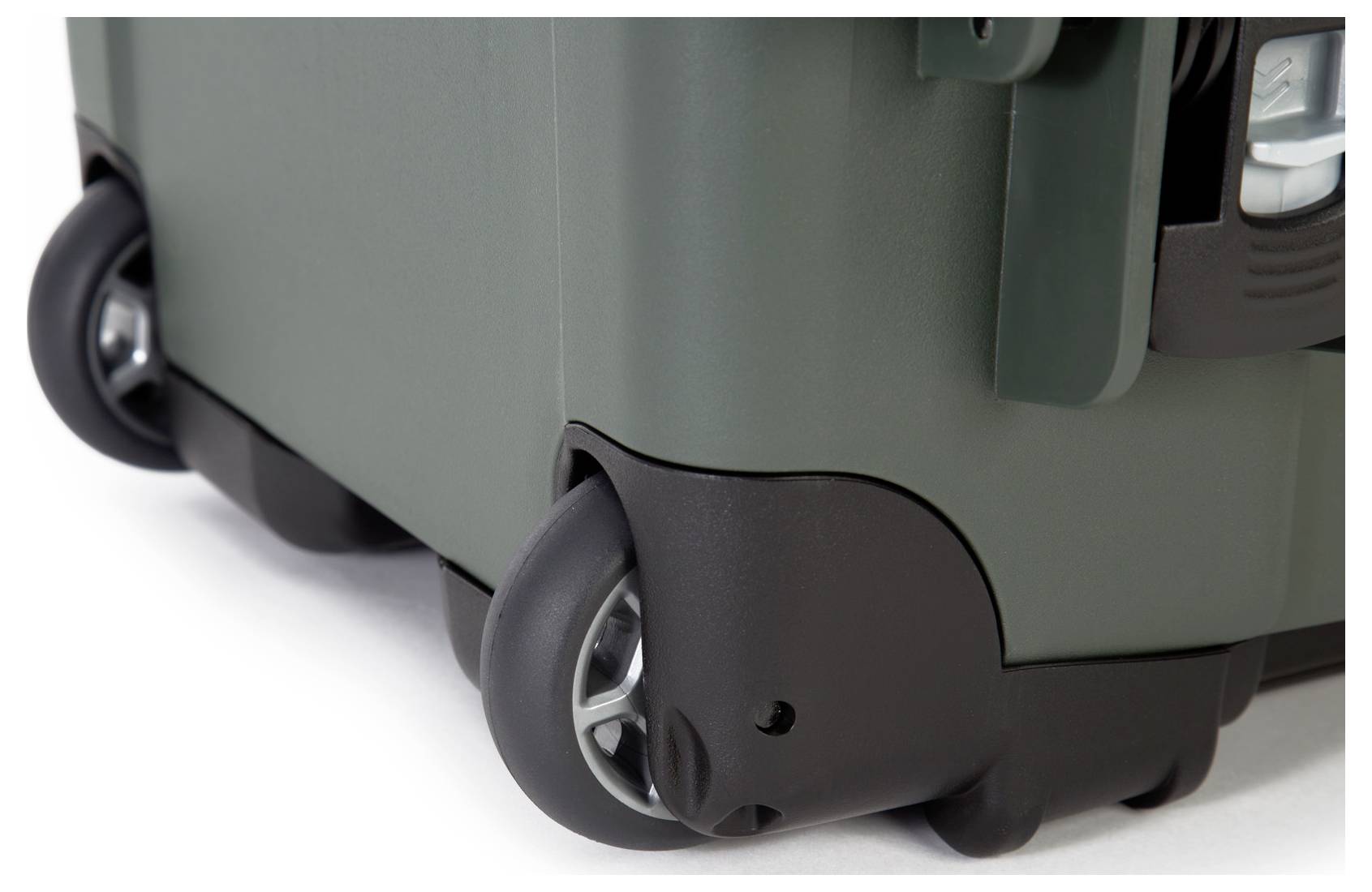 Kwadratowa, oliwkowozielona twarda walizka z czterema czarnymi kółkami, stojąca na białej powierzchni.