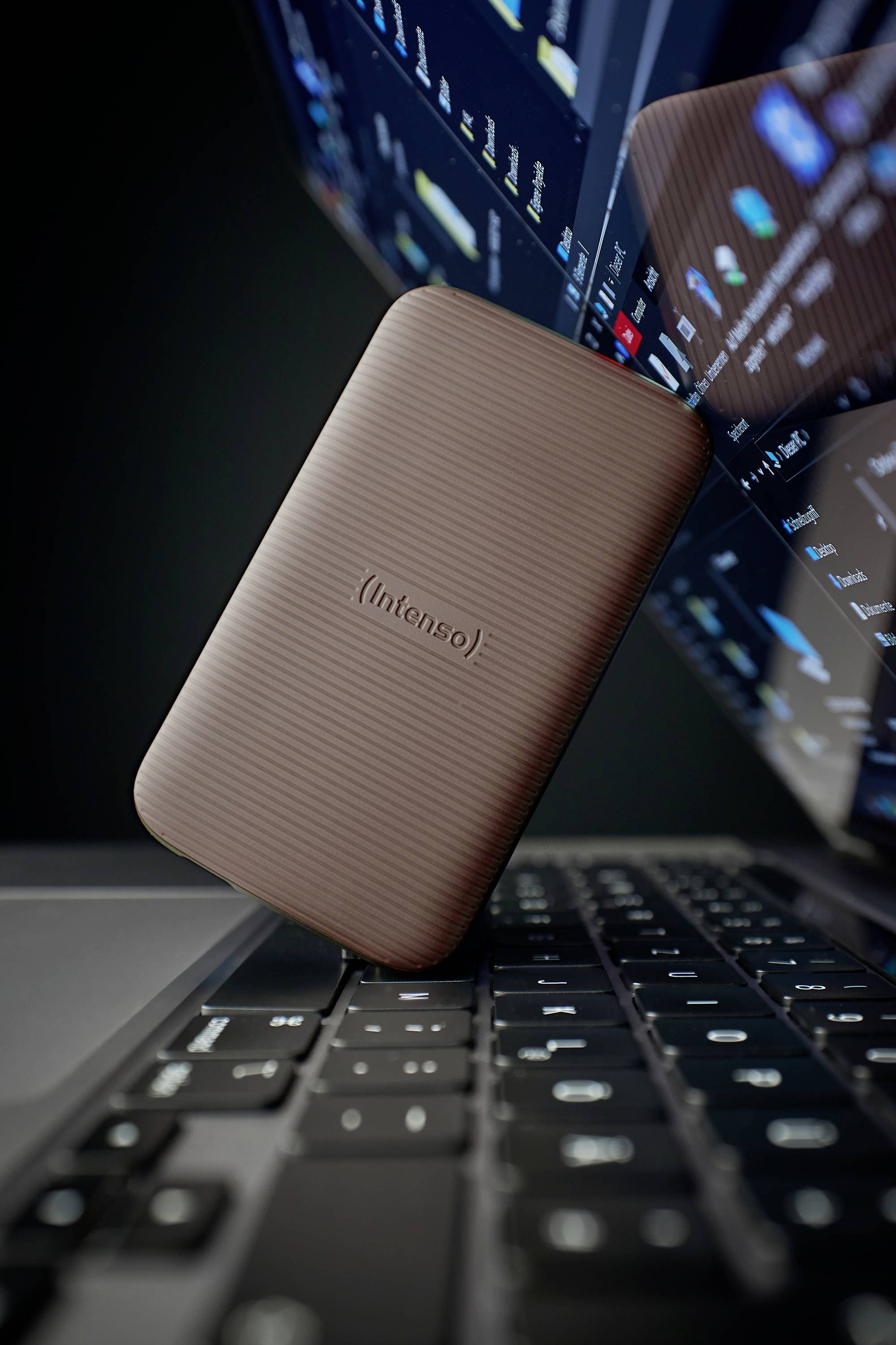 Zewnętrzny dysk twardy spoczywa na klawiaturze laptopa, otoczony widokami ekranu z cyfrowymi danymi.