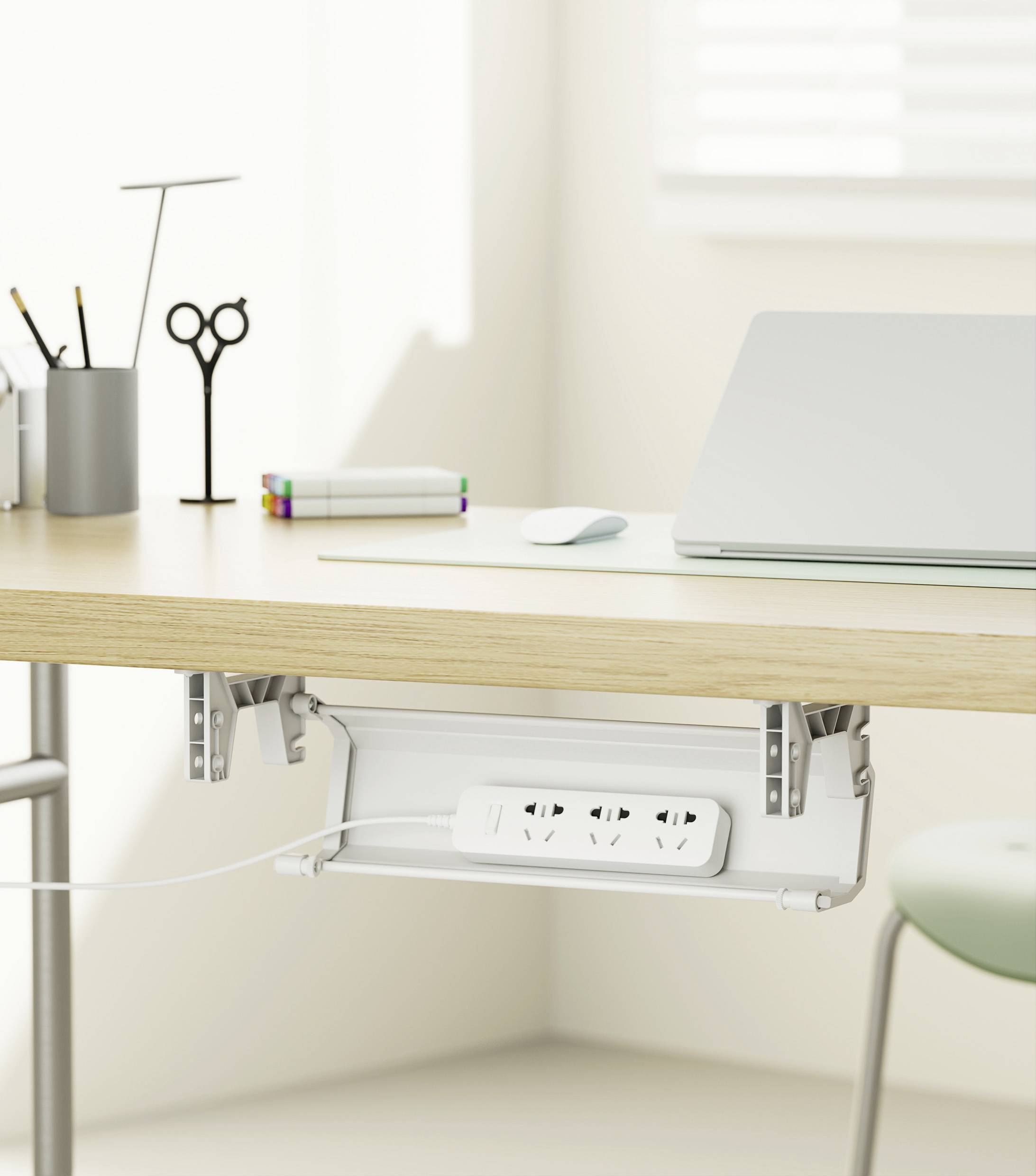 Jasna przestrzeń biurowa z biurkiem: Na wierzchu laptop, długopisy i notatniki, pod spodem listwa zasilająca, światło wpadające przez okno.