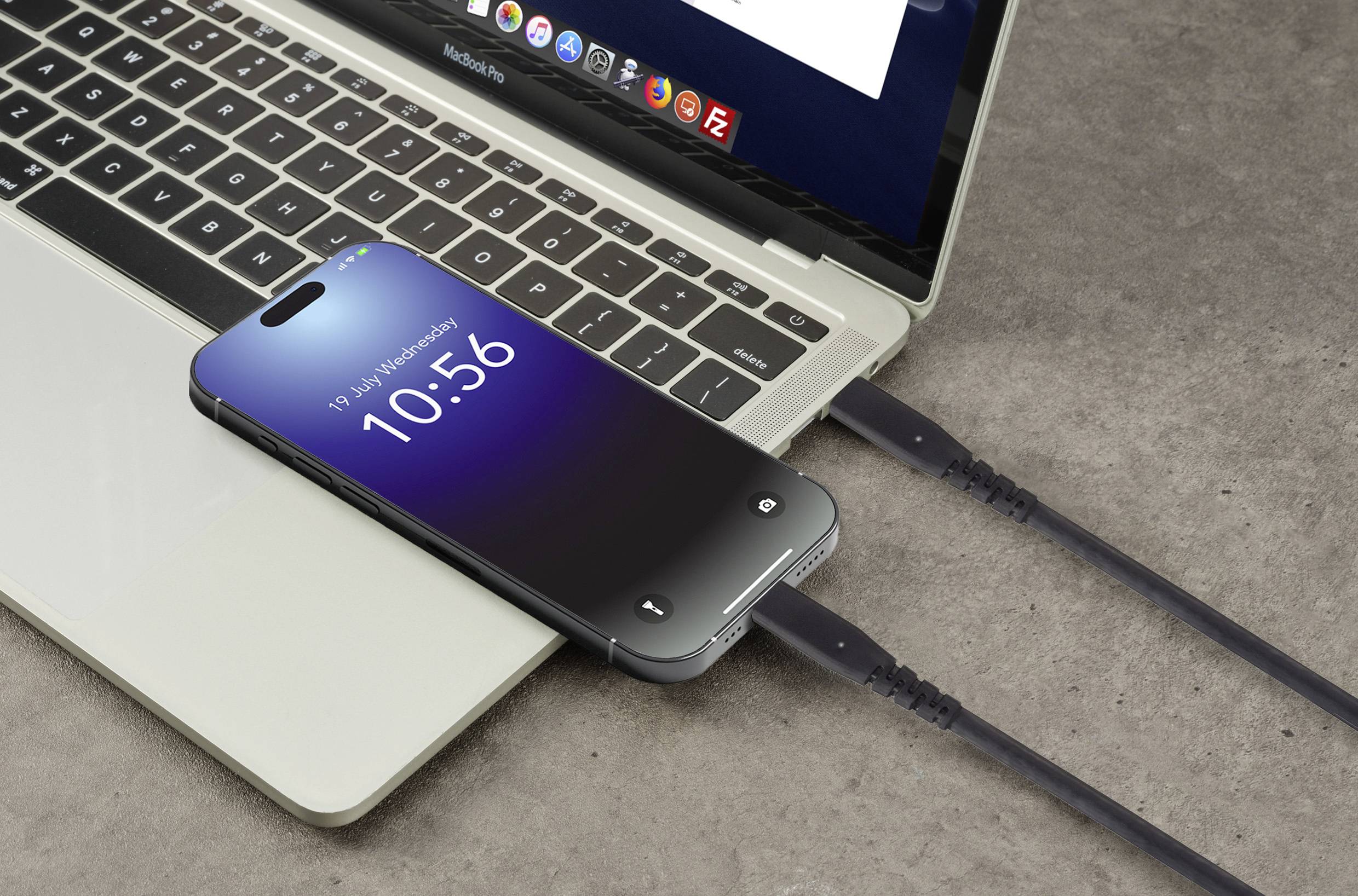 Smartfon leży na laptopie i jest ładowany przez kabel USB. Na ekranie wyświetlana jest godzina i data.