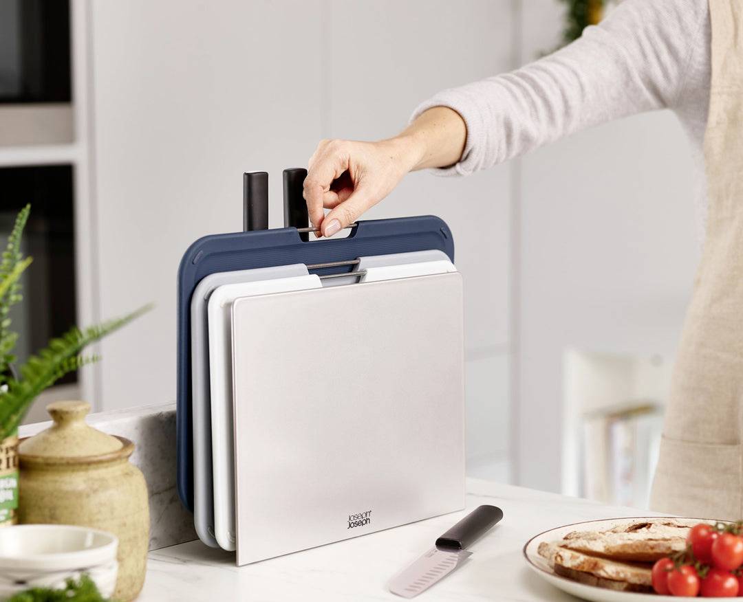 Osoba w kuchni wyjmuje deskę do krojenia z uchwytu. Na pierwszym planie leży nóż i pokrojony chleb.