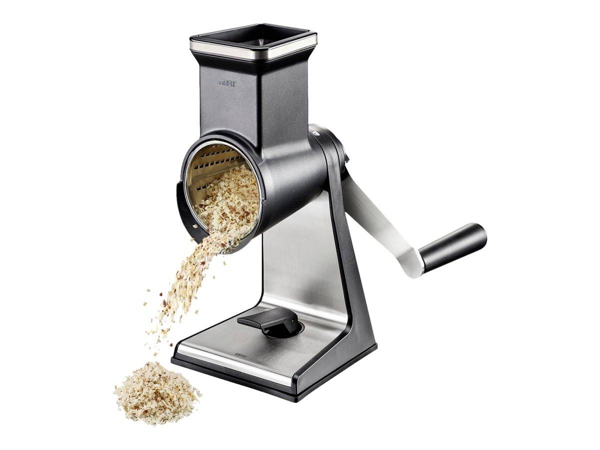 Ręczna metalowa tarka obrotowa z korbką, która wypuszcza starte produkty spożywcze przez otwór bębna, na białym tle.