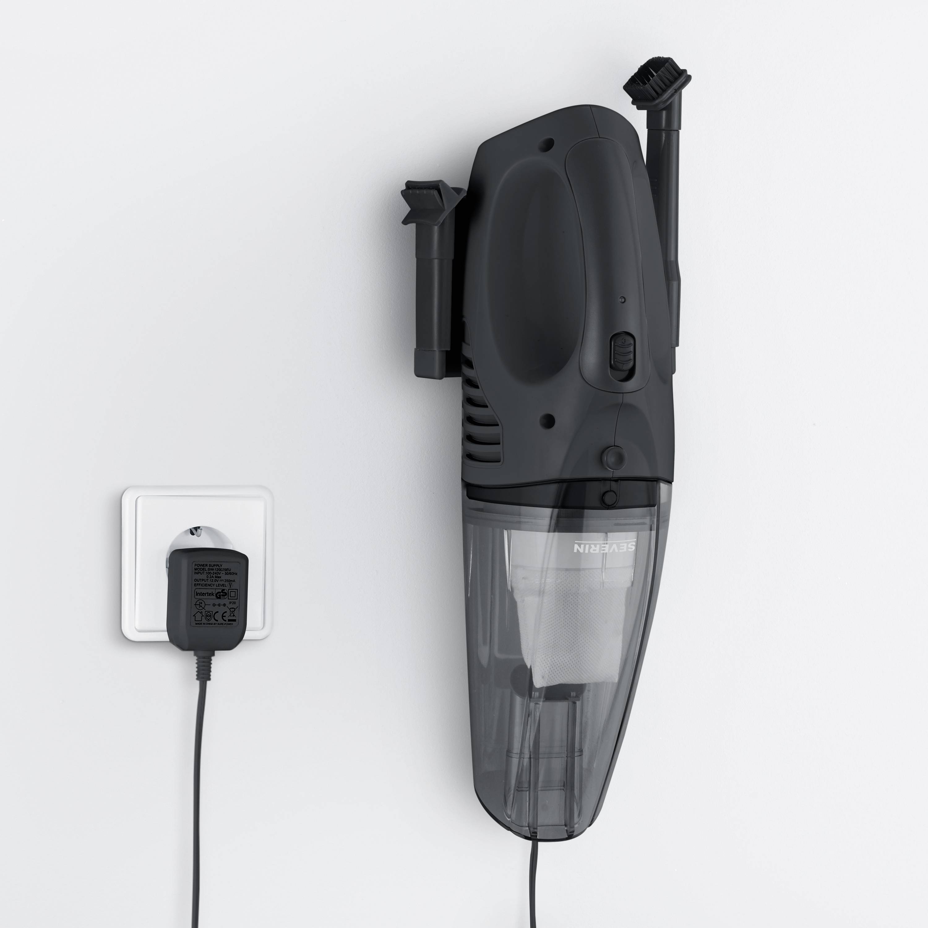 Bezprzewodowy odkurzacz ręczny wisi na ściennej stacji ładującej. Ładowarka jest podłączona do gniazdka elektrycznego.