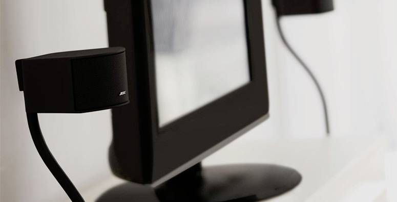 Monitor na stole, z dwoma głośnikami po bokach, w biurowym lub domowym miejscu pracy.