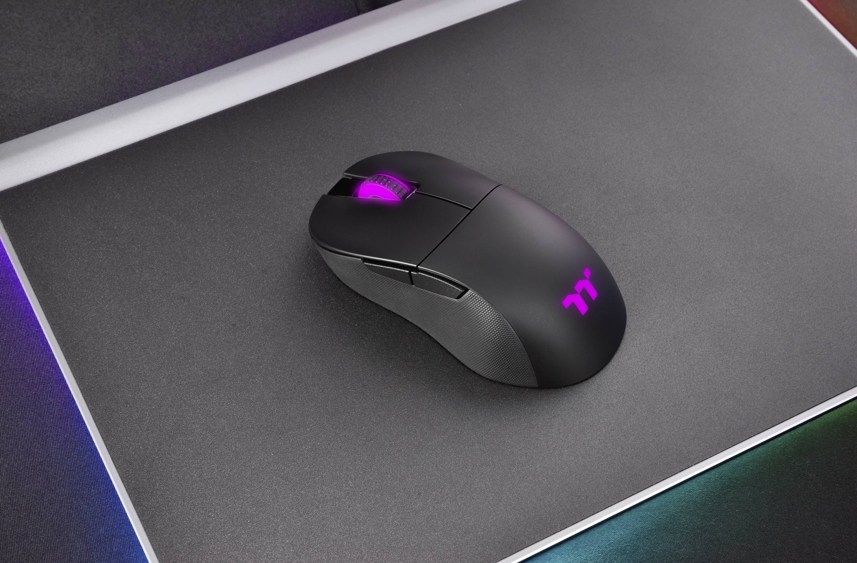 Bezprzewodowa mysz gamingowa z podświetlanym kółkiem scrollowania spoczywa na podkładce pod mysz. Logo na myszce również świeci.