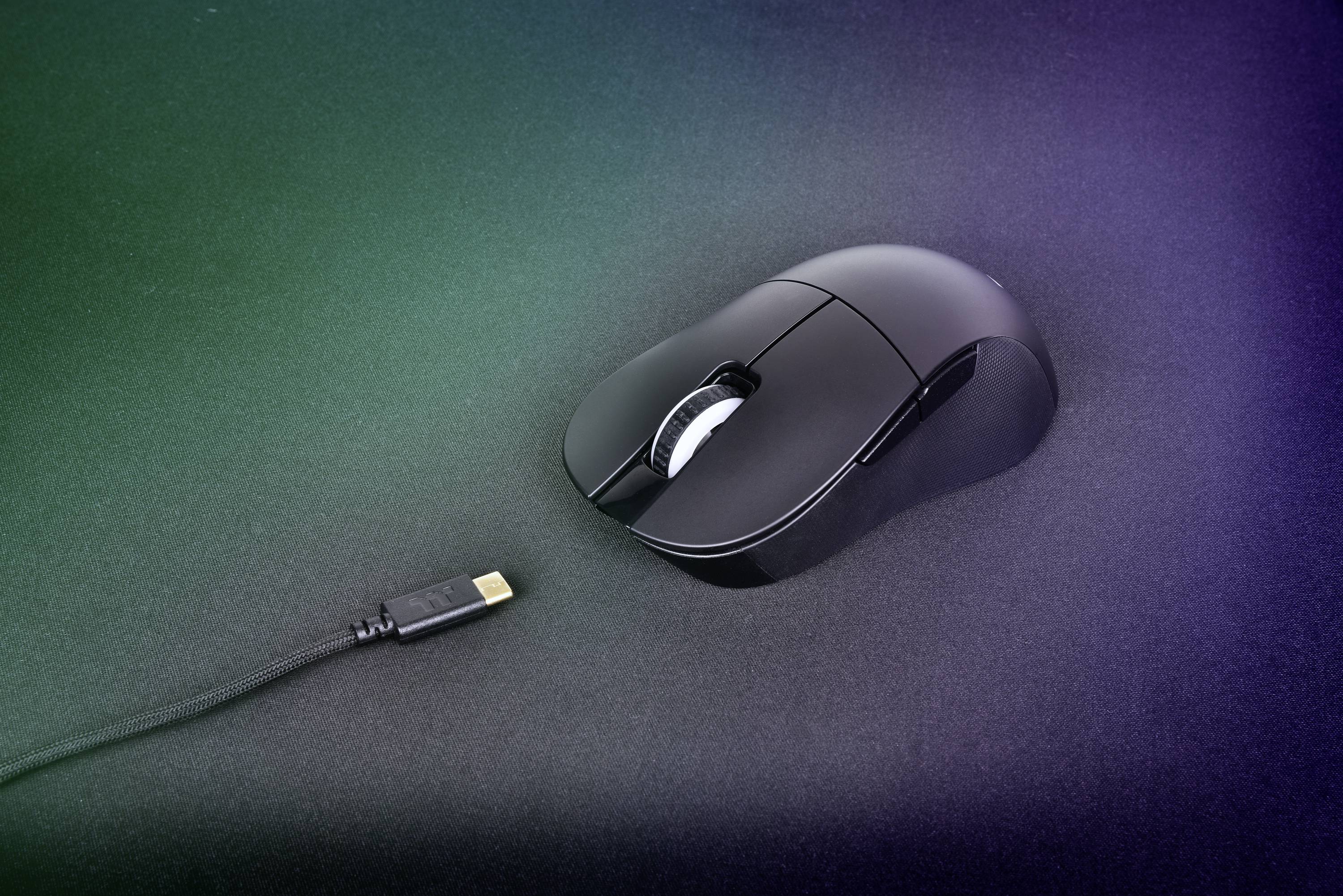 Osoba steruje myszą komputerową RGB lewą ręką obok podświetlonej klawiatury na ciemnym stole.