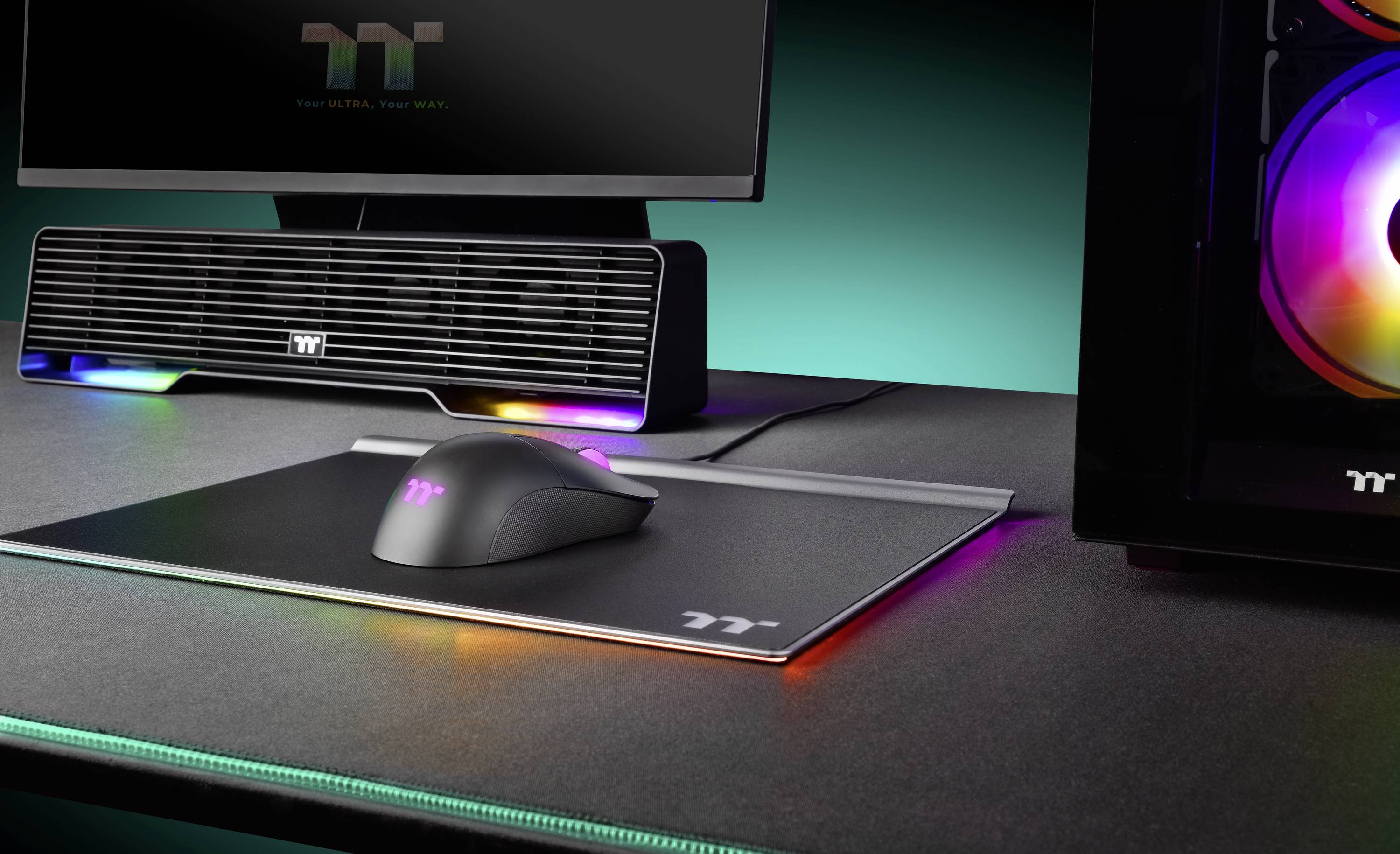 Nowoczesny stół komputerowy z monitorem, podświetloną myszą gamingową na podkładce oraz obudową komputera z kolorowymi światłami.