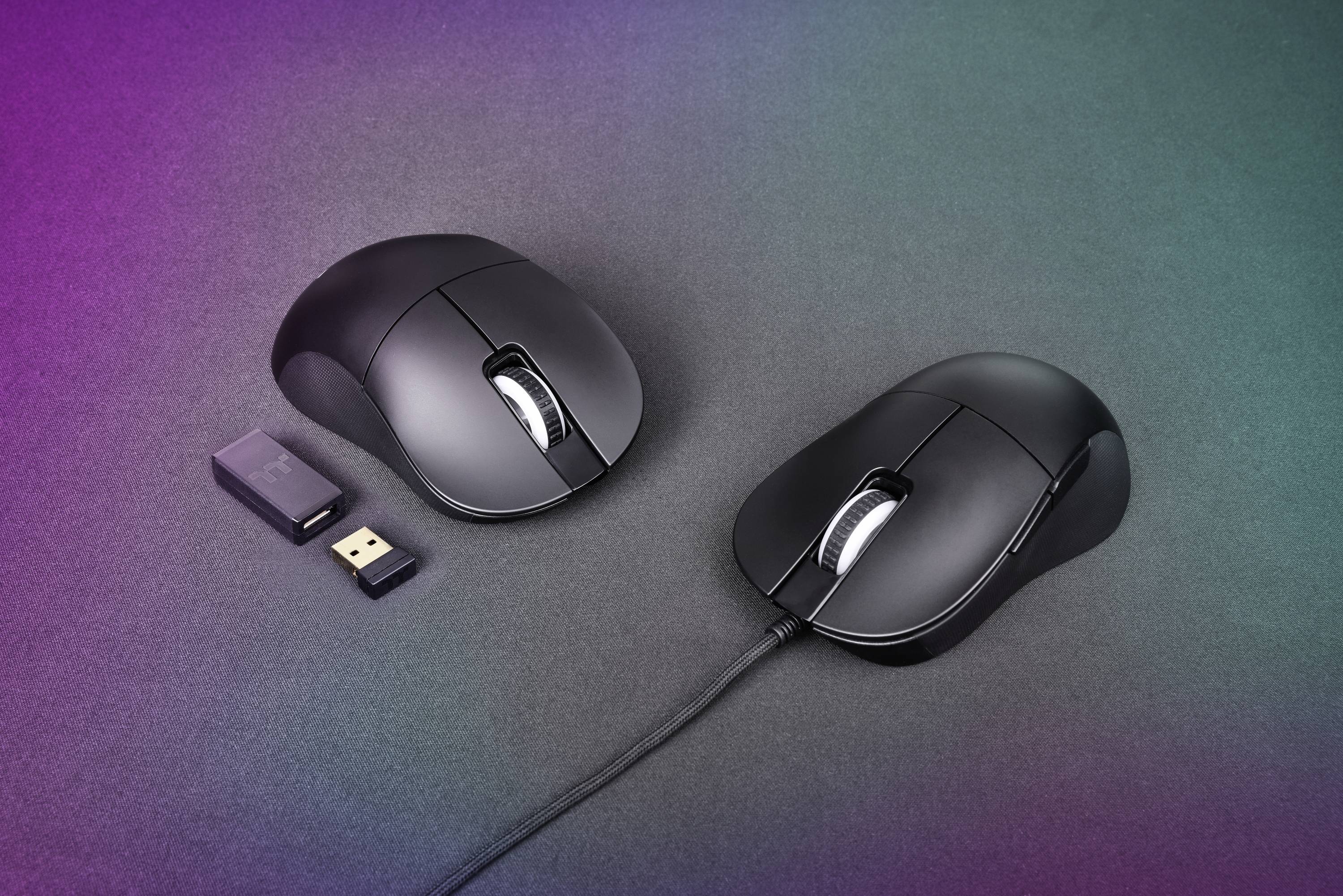 Dwie czarne myszki komputerowe, jedna bezprzewodowa z odbiornikiem USB, druga przewodowa, na fioletowo-zielonym tle.