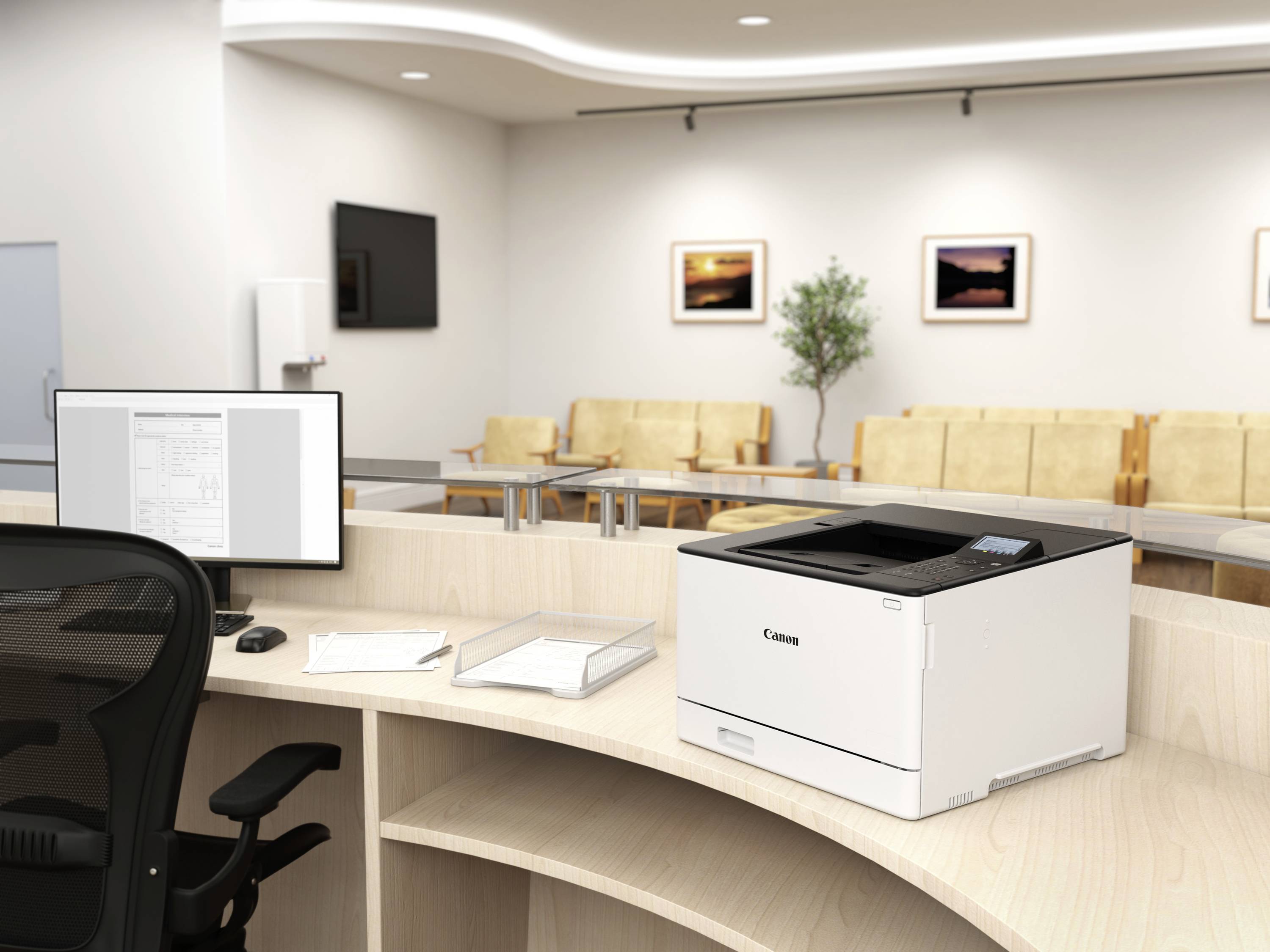 Nowoczesna drukarka stoi na biurku w biurze, obok ekranu komputera, pustych krzeseł i dekoracji ściennych w tle.