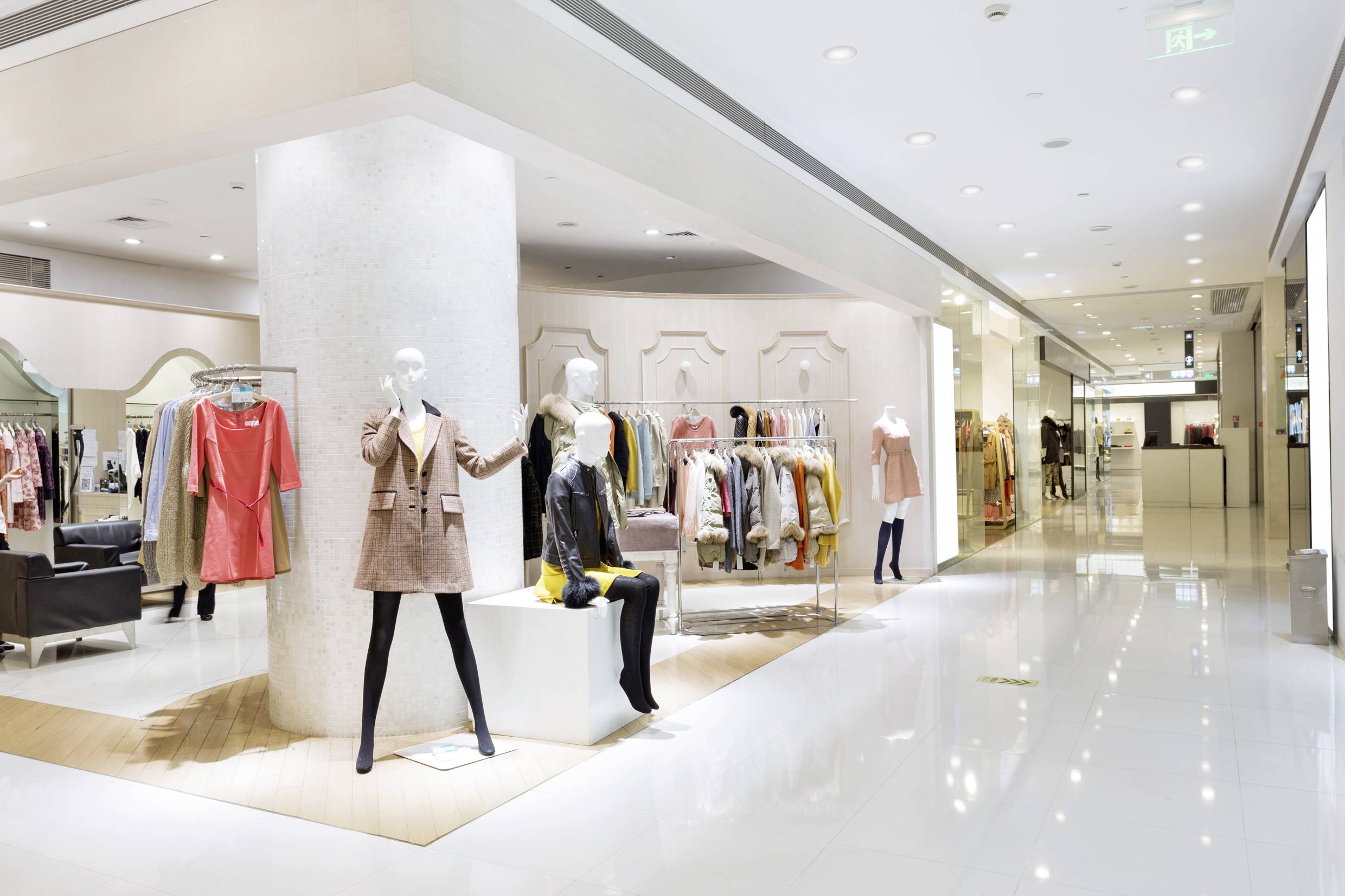 Nowoczesny sklep odzieżowy z manekinami prezentującymi różne ubrania. W tle widoczne są półki z kolejnymi artykułami odzieżowymi.