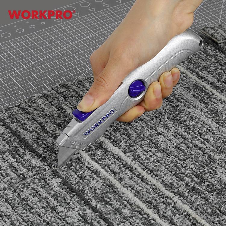 Ręka trzyma szare nożyce tapicerskie i przecina szary, strukturalny dywan, który leży na macie do cięcia.