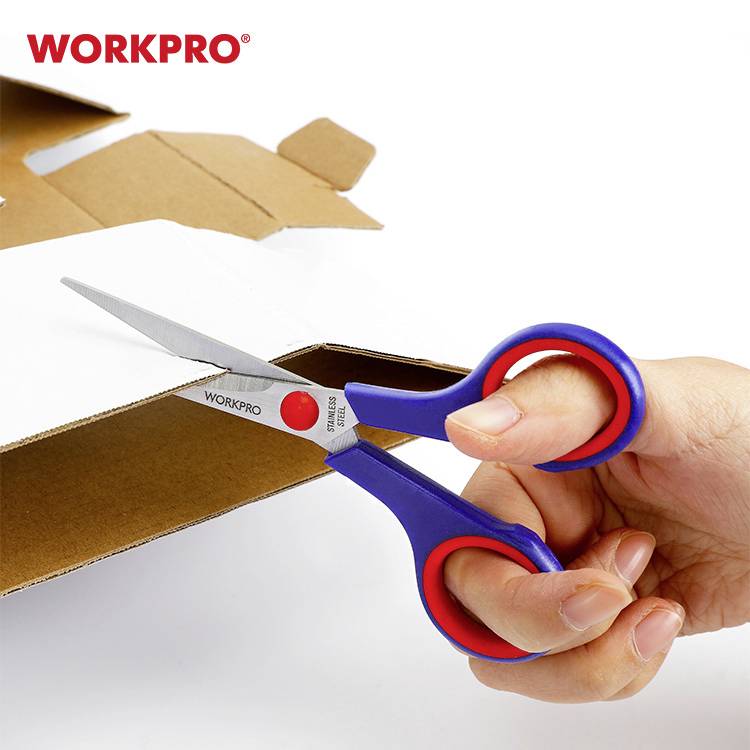 Jedna ręka trzyma niebieskie i czerwone nożyczki i przycina tekturę. W tle pudełko z napisem 'WORKPRO'.