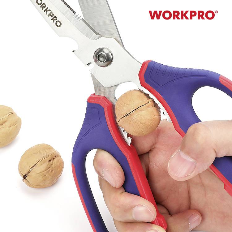 Osoba trzyma niebieskie i czerwone szczypce marki 'WORKPRO' i łamie orzech włoski. Obok leżą dwa kolejne orzechy włoskie.