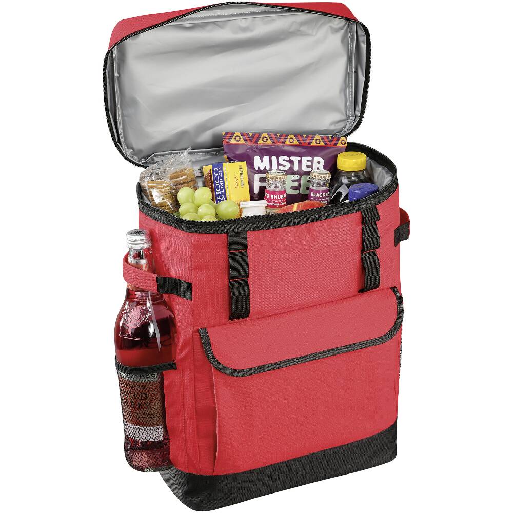 Czerwony plecak piknikowy z otwartą kieszenią, wypełniony jedzeniem, sokiem, ciastkami, winogronami i butelką lemoniady w bocznej kieszeni.