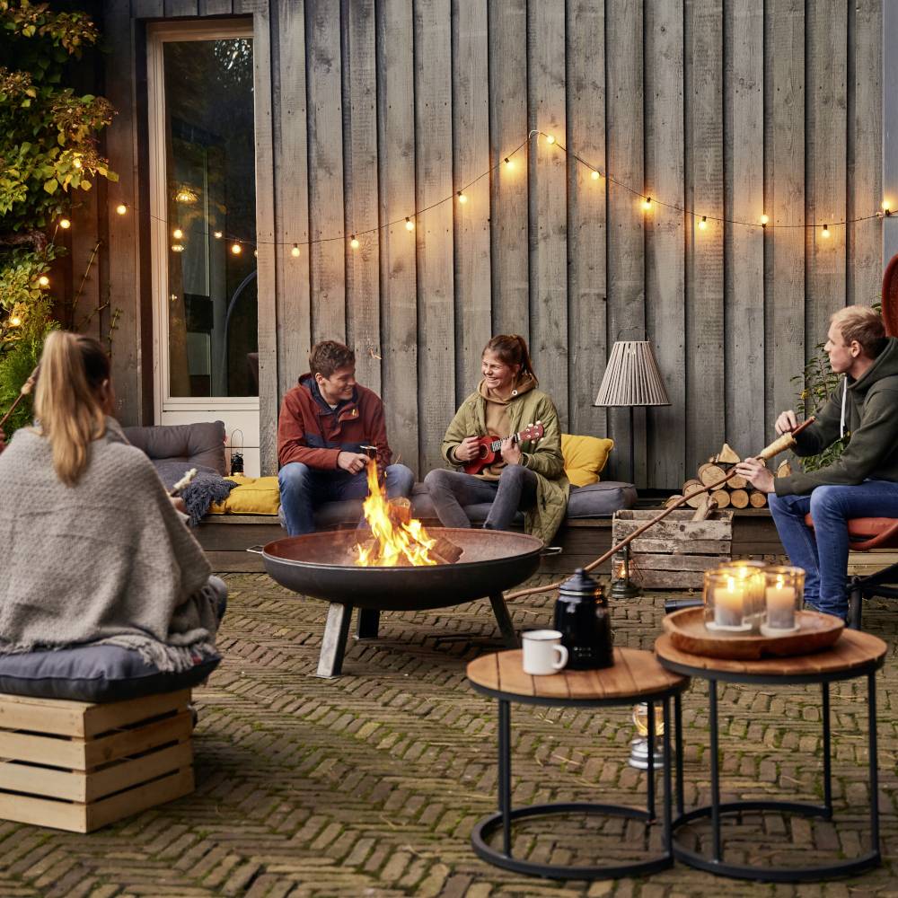 Cztery osoby siedzą na dworze wokół ogniska. Rozmawiają i relaksują się w przytulnym świetle.
