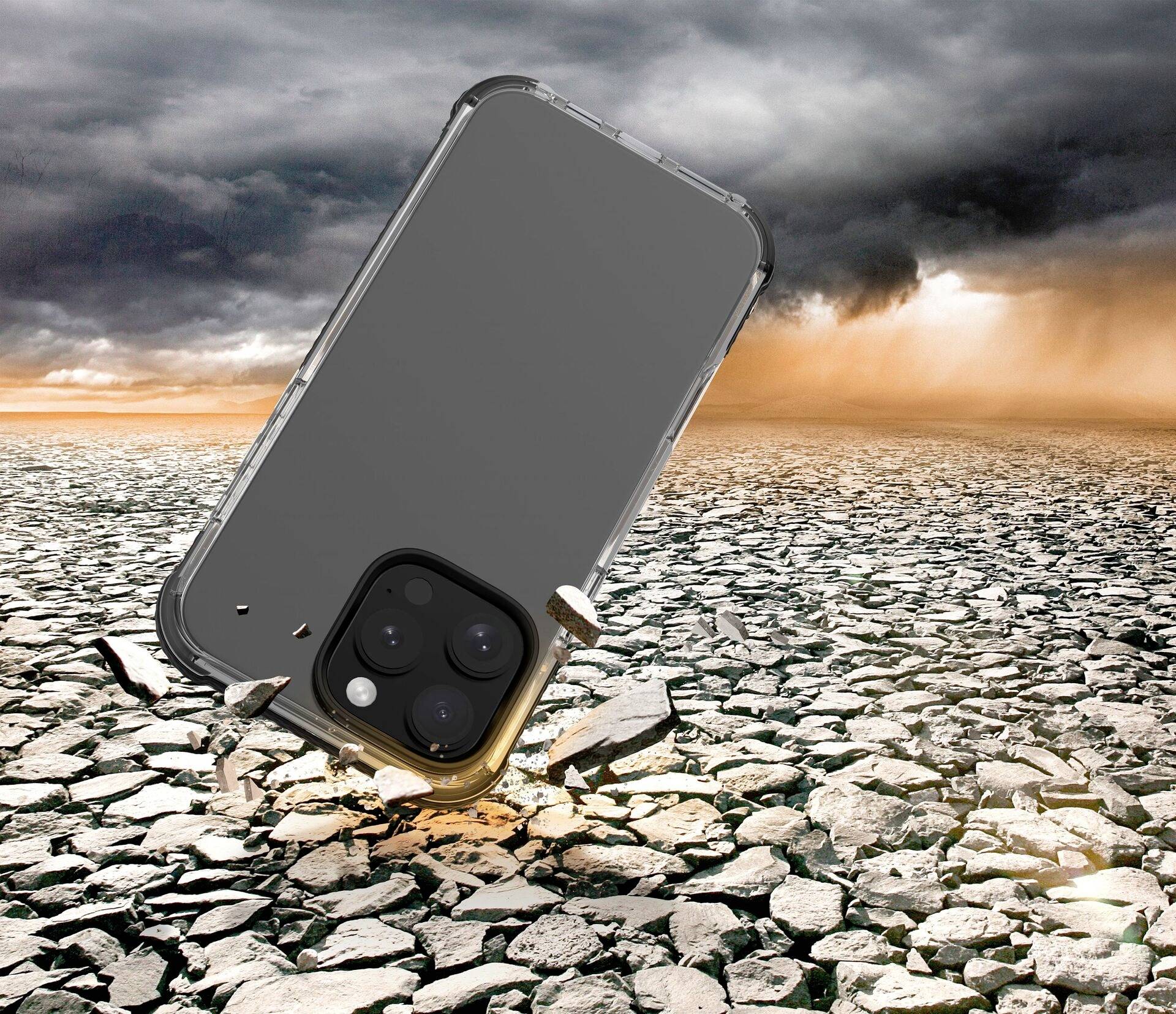 Smartfon w etui spada na suchą, popękaną pustynną przestrzeń. W tle unoszą się chmury i pył.