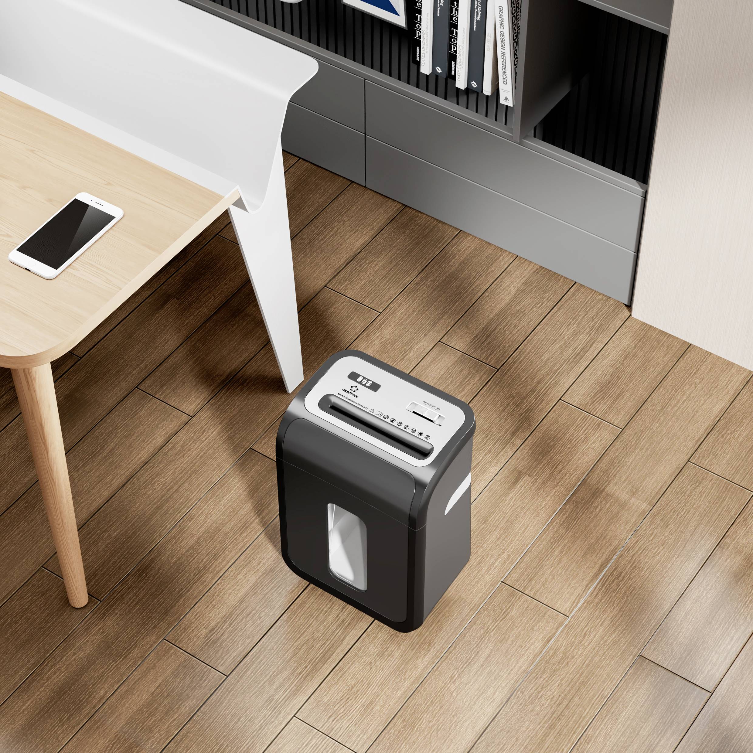 Niszczarka dokumentów stoi na drewnianej podłodze obok biurka z telefonem komórkowym na wierzchu. W tle widoczne są regały.