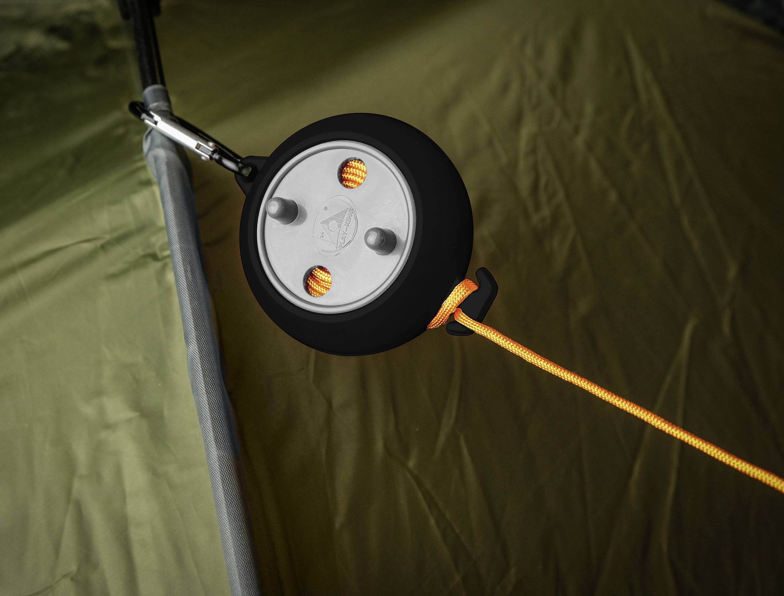 Namiot z pomarańczowym sznurem przewleczonym przez okrągły uchwyt, pozwalający na regulację naprężenia linki namiotu.