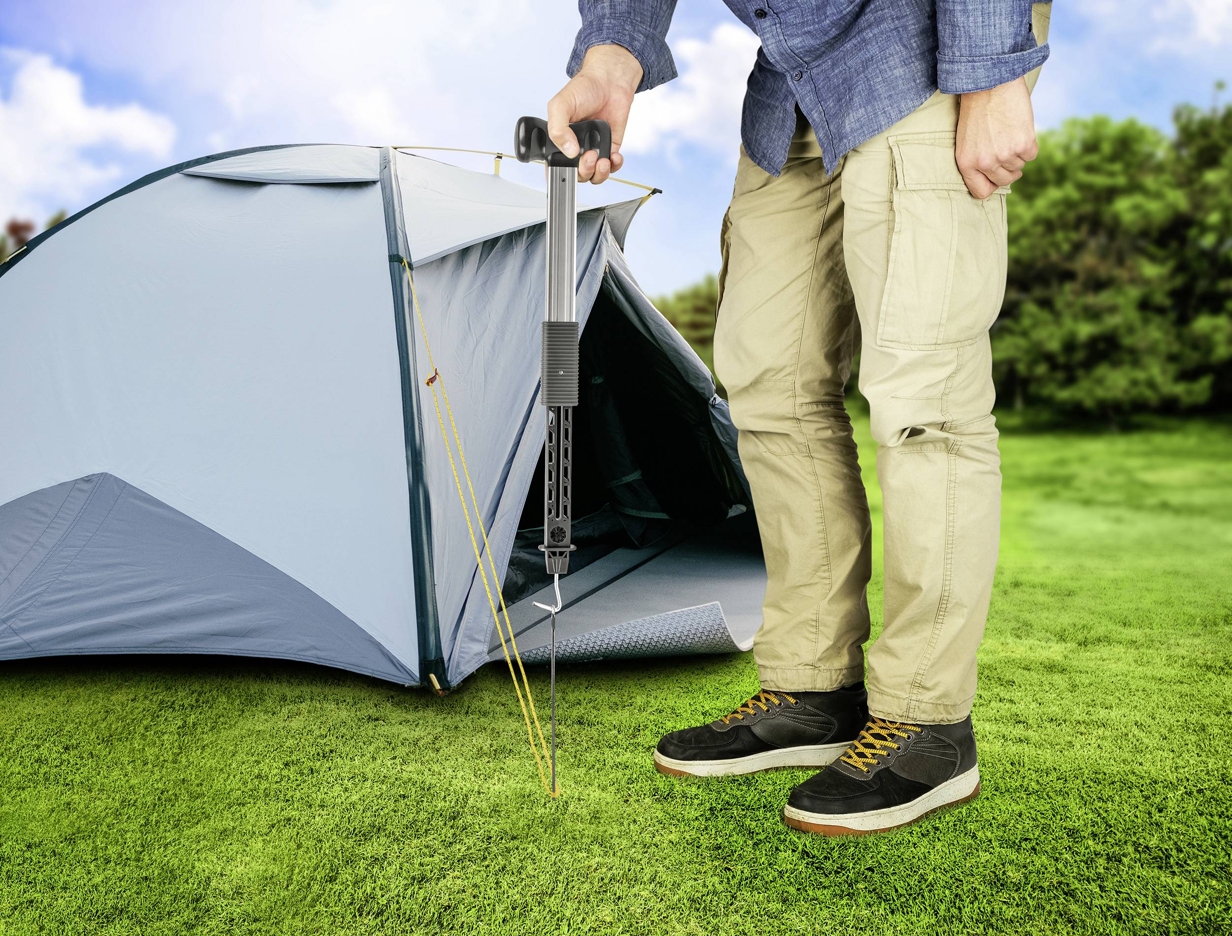 Osoba napina namiot za pomocą narzędzia naciągającego na zielonej trawie. Namiot jest niebieski, a niebo jest czyste.