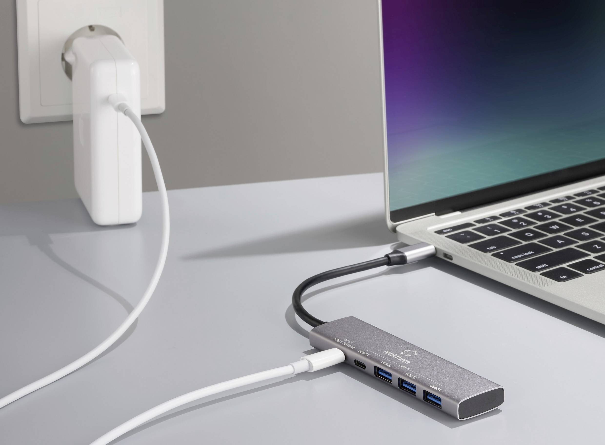 Laptop podłączony do koncentratora USB-C, który jest podłączony do gniazdka elektrycznego. Hub posiada kilka złączy, w tym porty USB.
