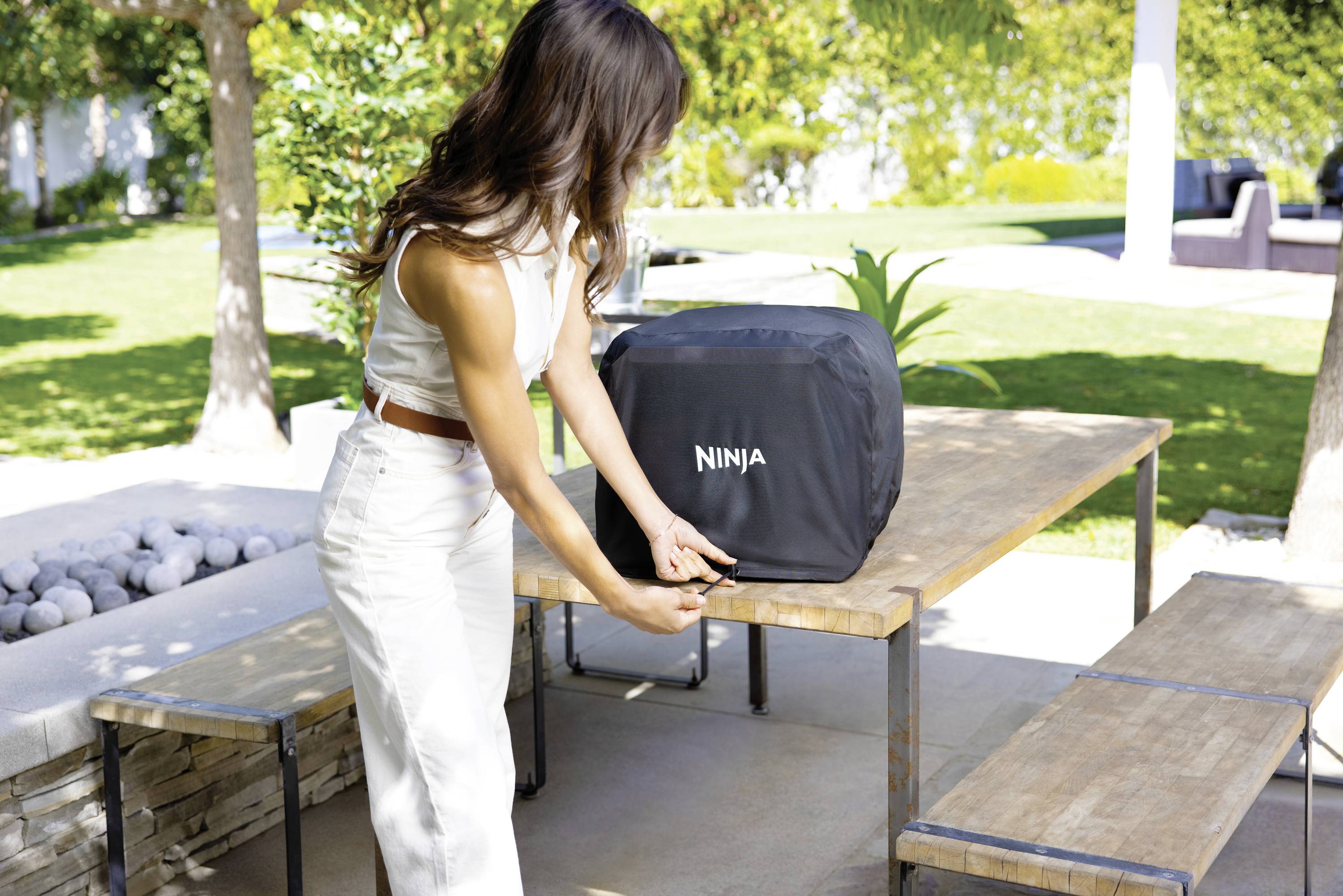Kobieta mocuje zamek błyskawiczny na pokrowcu z napisem 'Ninja' na drewnianym stole w słonecznym ogrodzie.