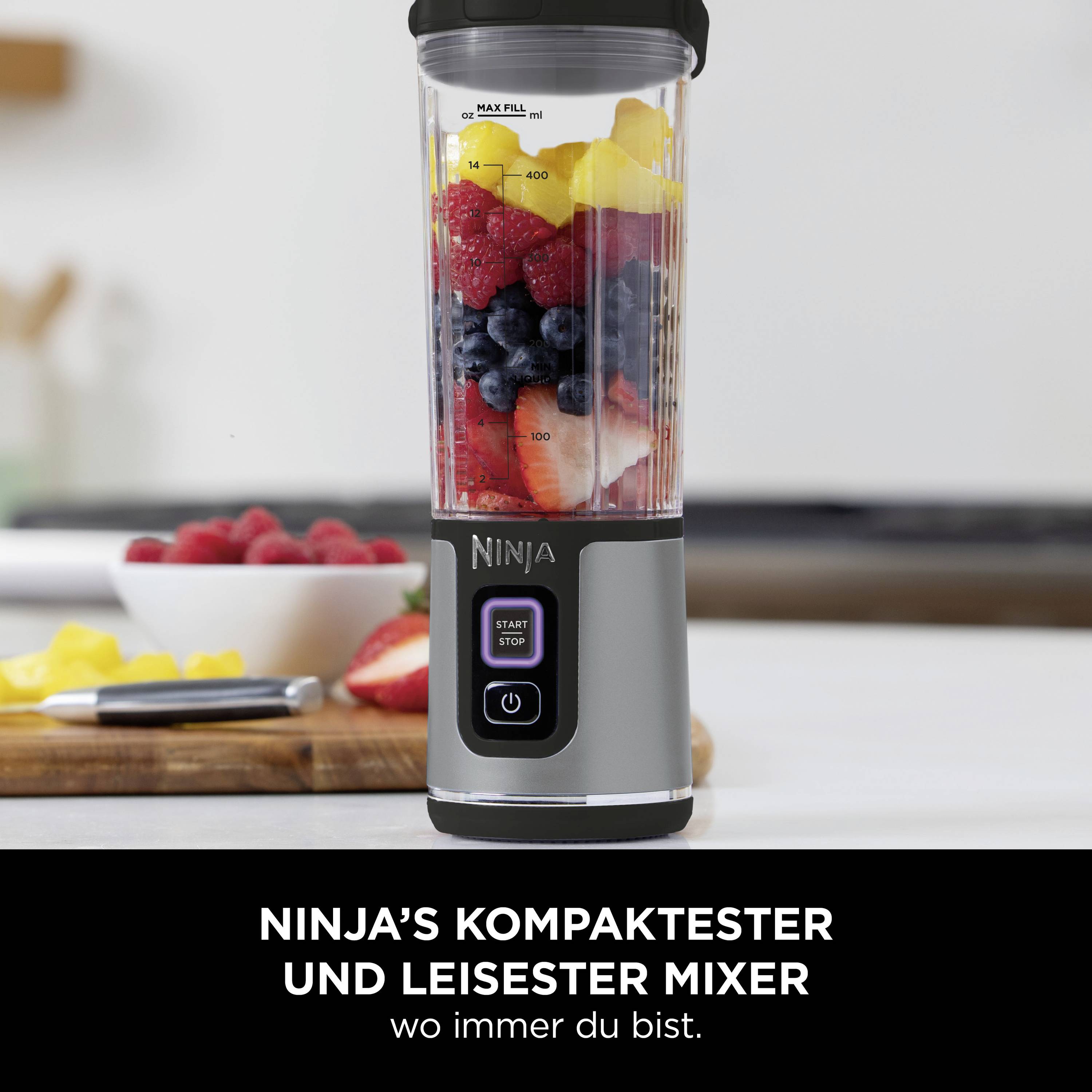 Na stole kuchennym stoi urządzenie do miksowania, napełnione owocami takimi jak banany, jagody i mango. Tekst poniżej: 'Najpompaktowszy i najcichszy blender Ninja, jaki możesz mieć gdziekolwiek.'
