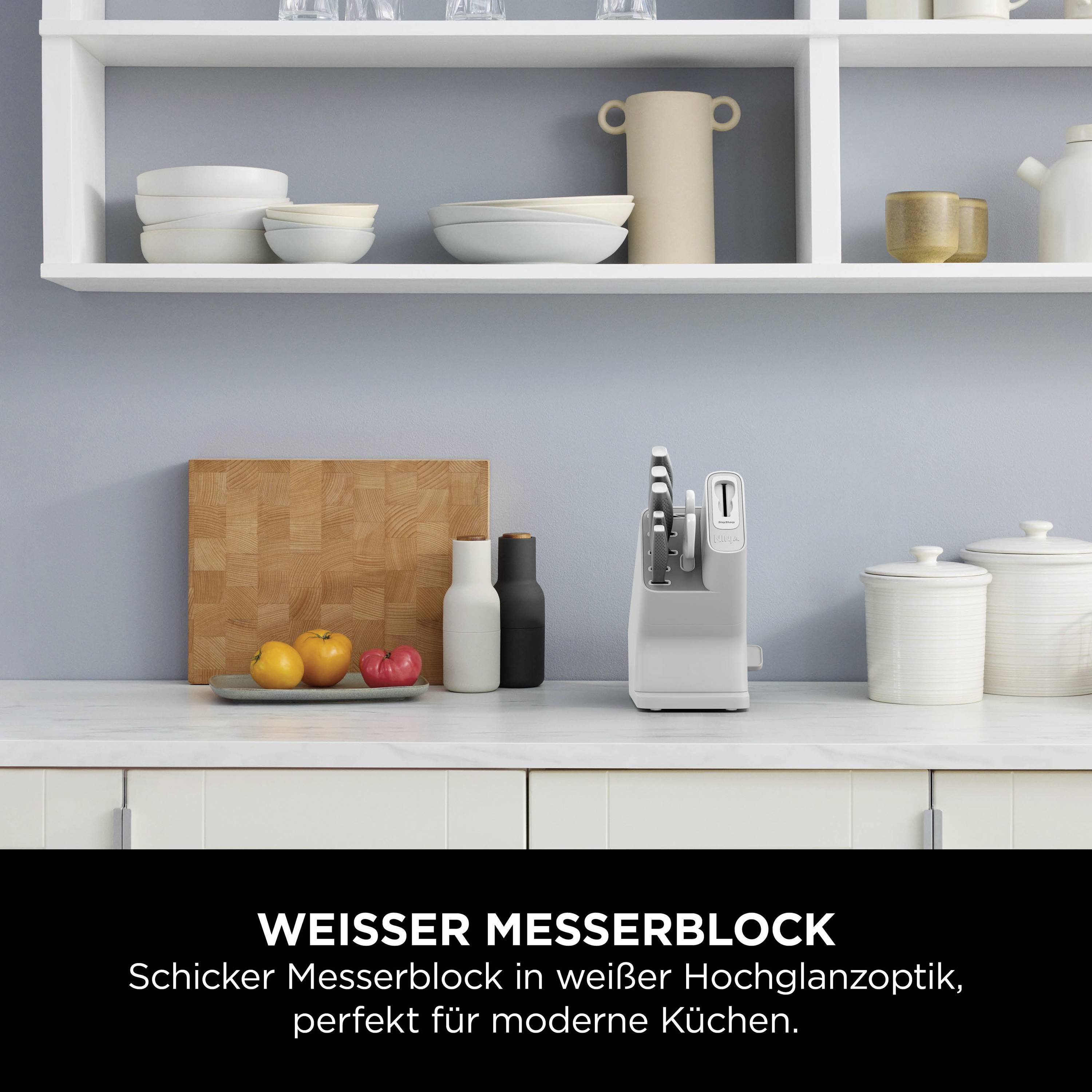 Biały blok na noże z kilkoma nożami stoi na blacie kuchennym. W tle widoczne są półki z naczyniami.