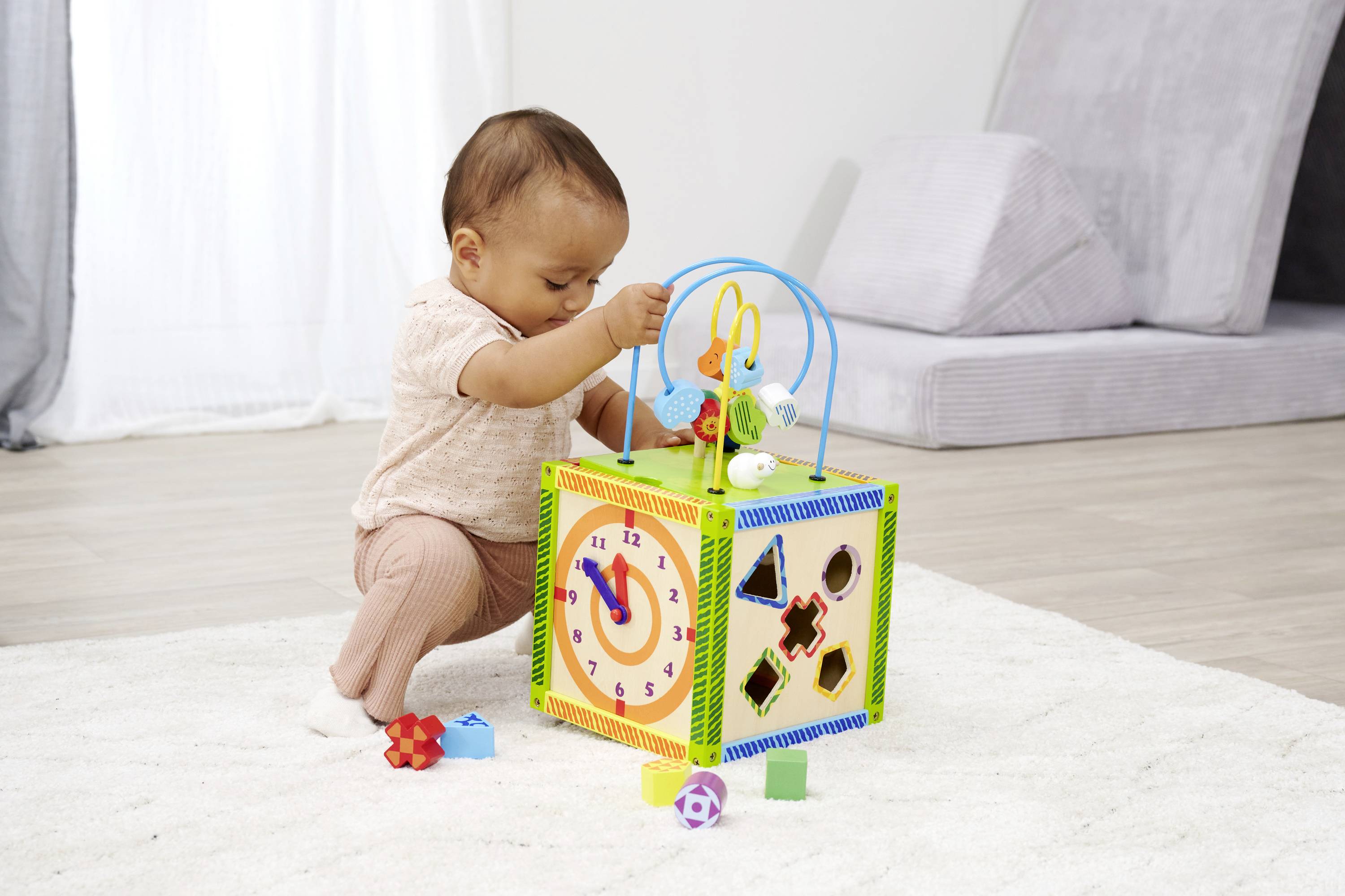 Małe dziecko bawi się na dywanie kolorową kostką manipulacyjną, która oferuje różne kształty do wsadzania i obracania.