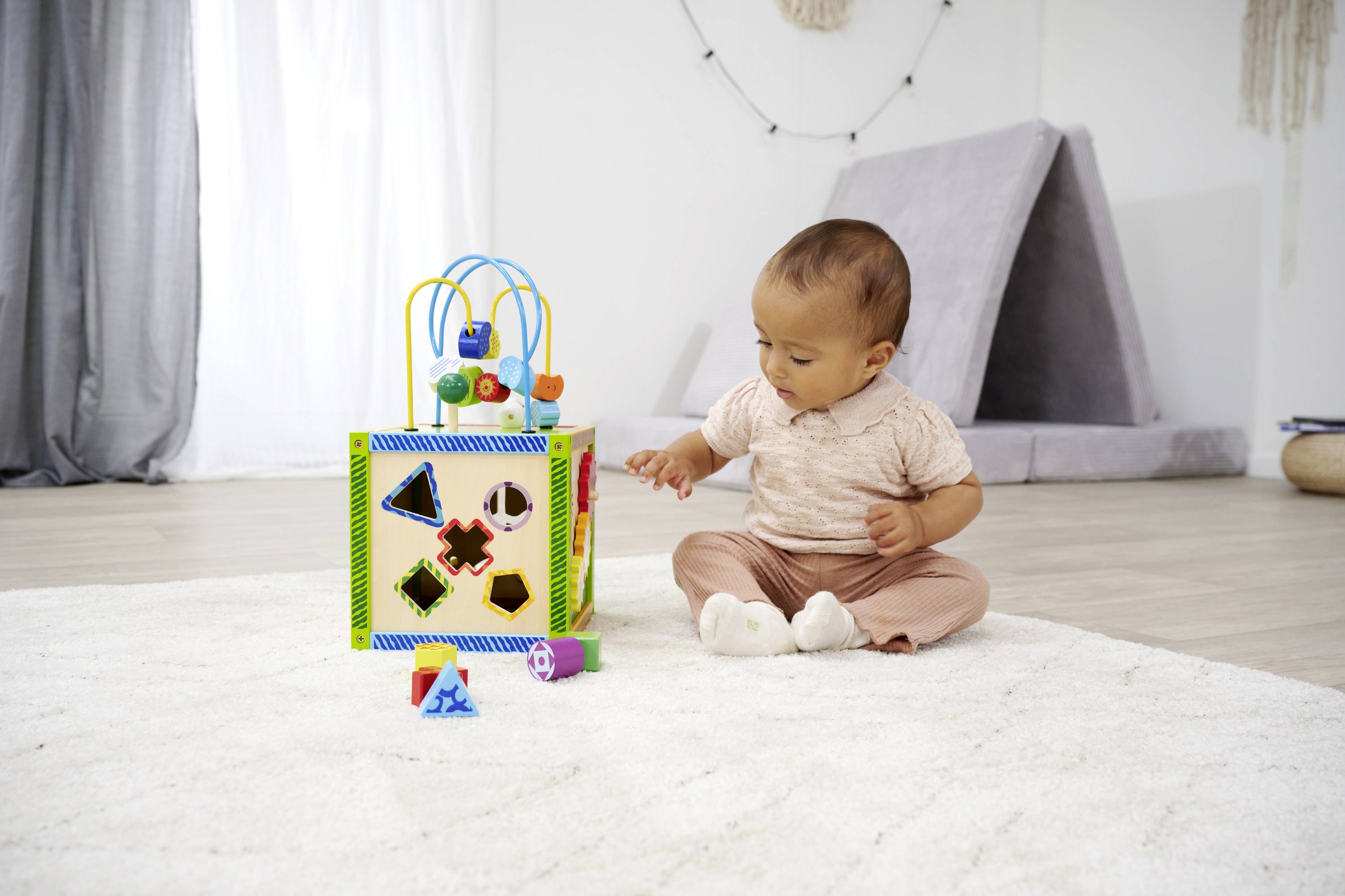 Małe dziecko siedzi na dywanie i bawi się kolorową, wielofunkcyjną kostką manipulacyjną, otoczone jasną, przyjazną przestrzenią.