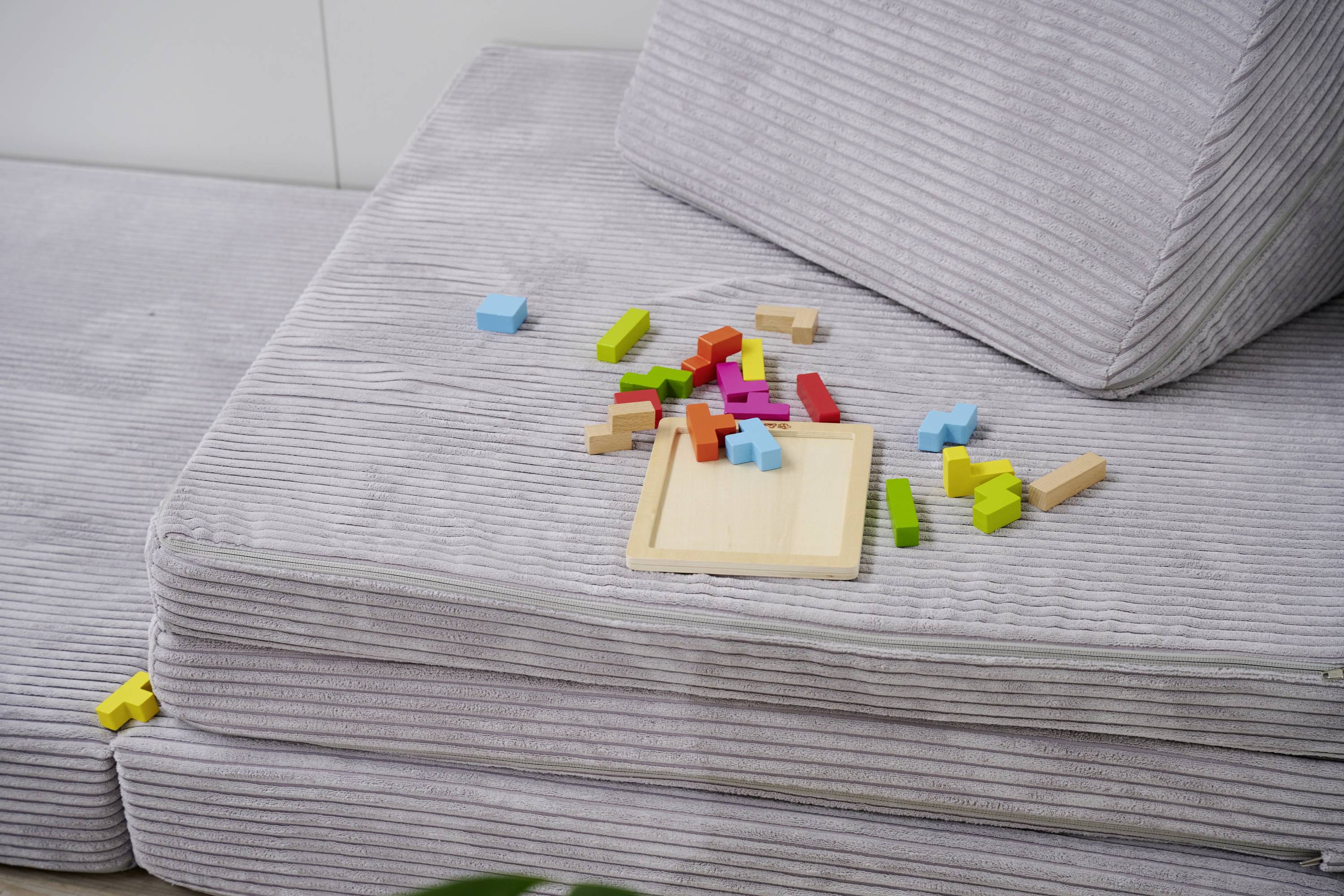 Kolorowe drewniane klocki są rozrzucone na szarej kanapie.