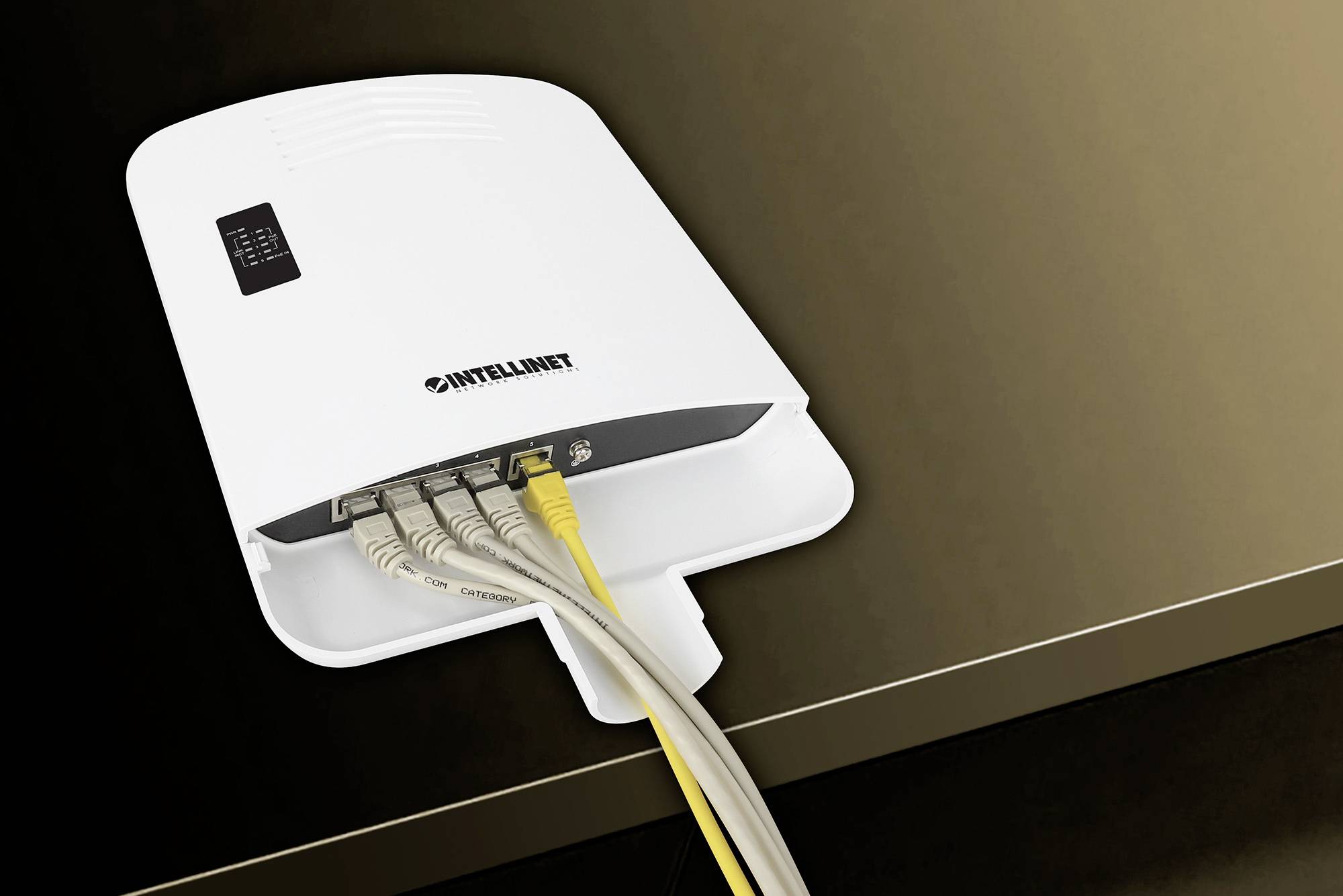 Biały switch sieciowy z czterema podłączonymi kablami Ethernet, zamontowany na ścianie.