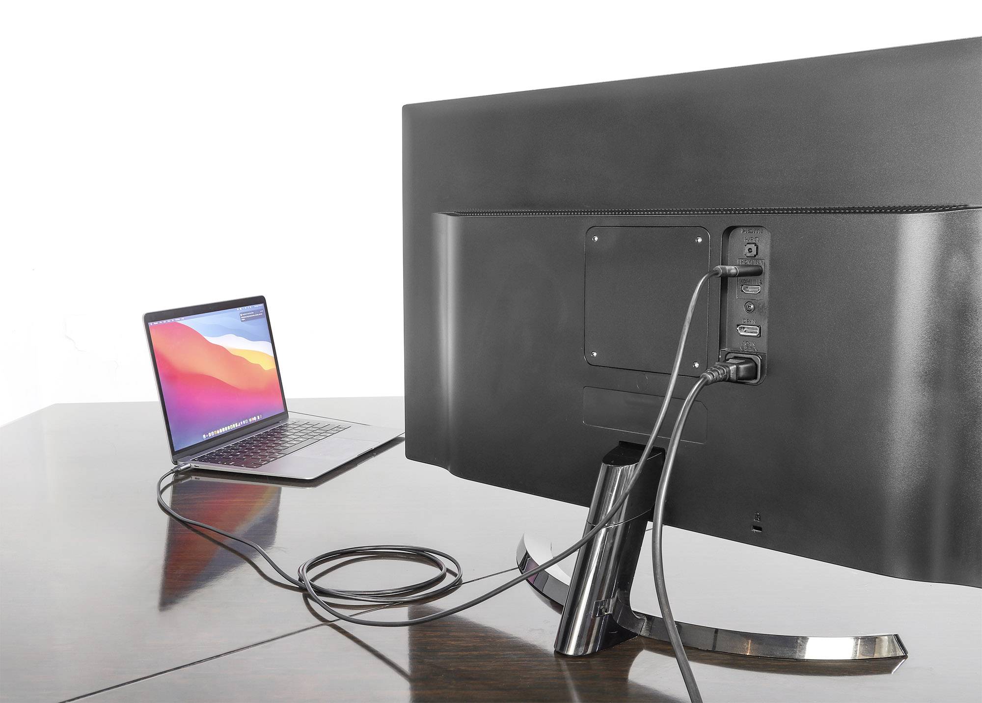 Laptop jest podłączony do dużego monitora, oba stoją na drewnianym stole. Na ekranie nie widać, co jest wyświetlane.