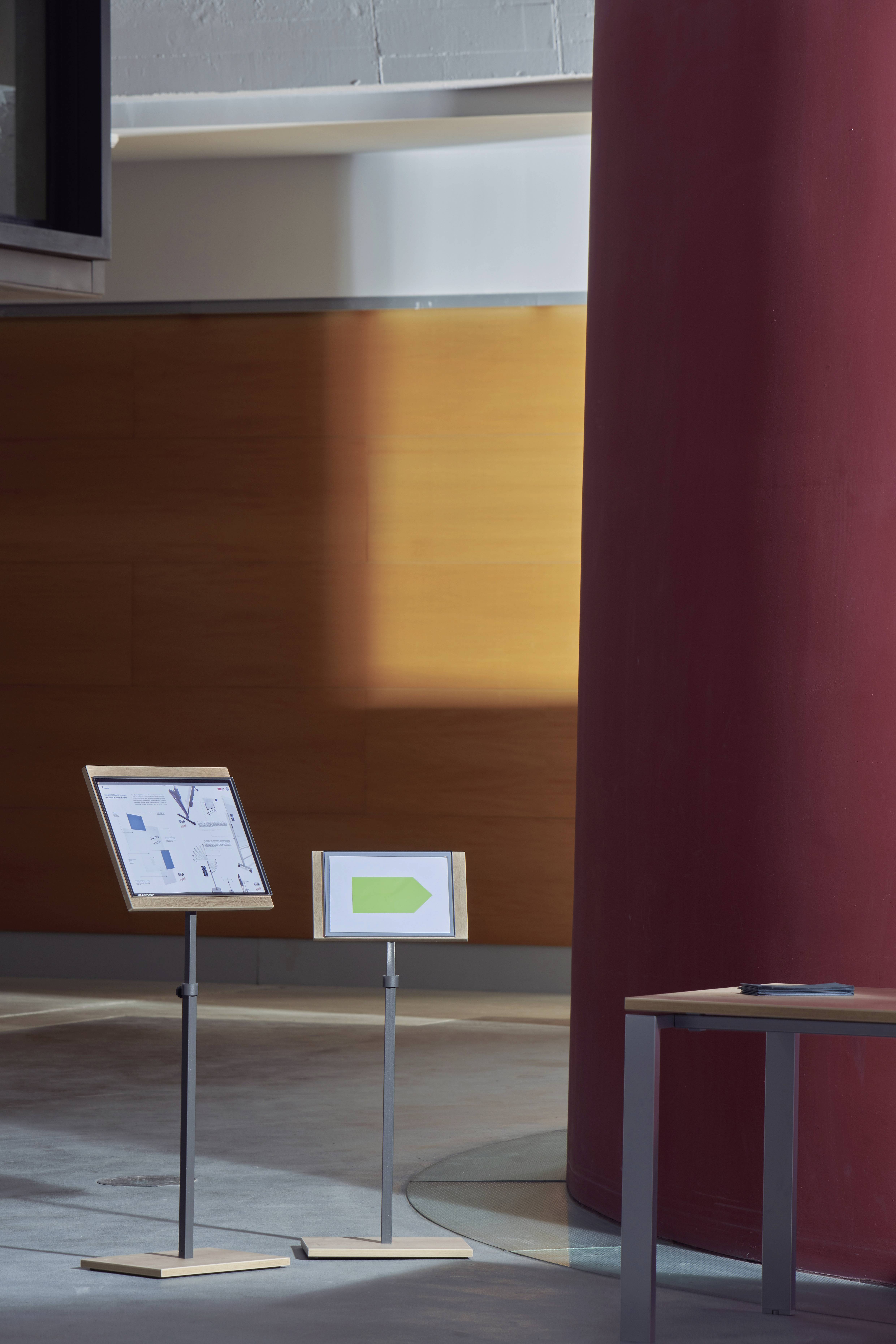 'Dwie tablice stoją w nowoczesnej hali. Po lewej stronie mały plan poglądowy, po prawej stronie tabliczka z zielonym strzałką.'