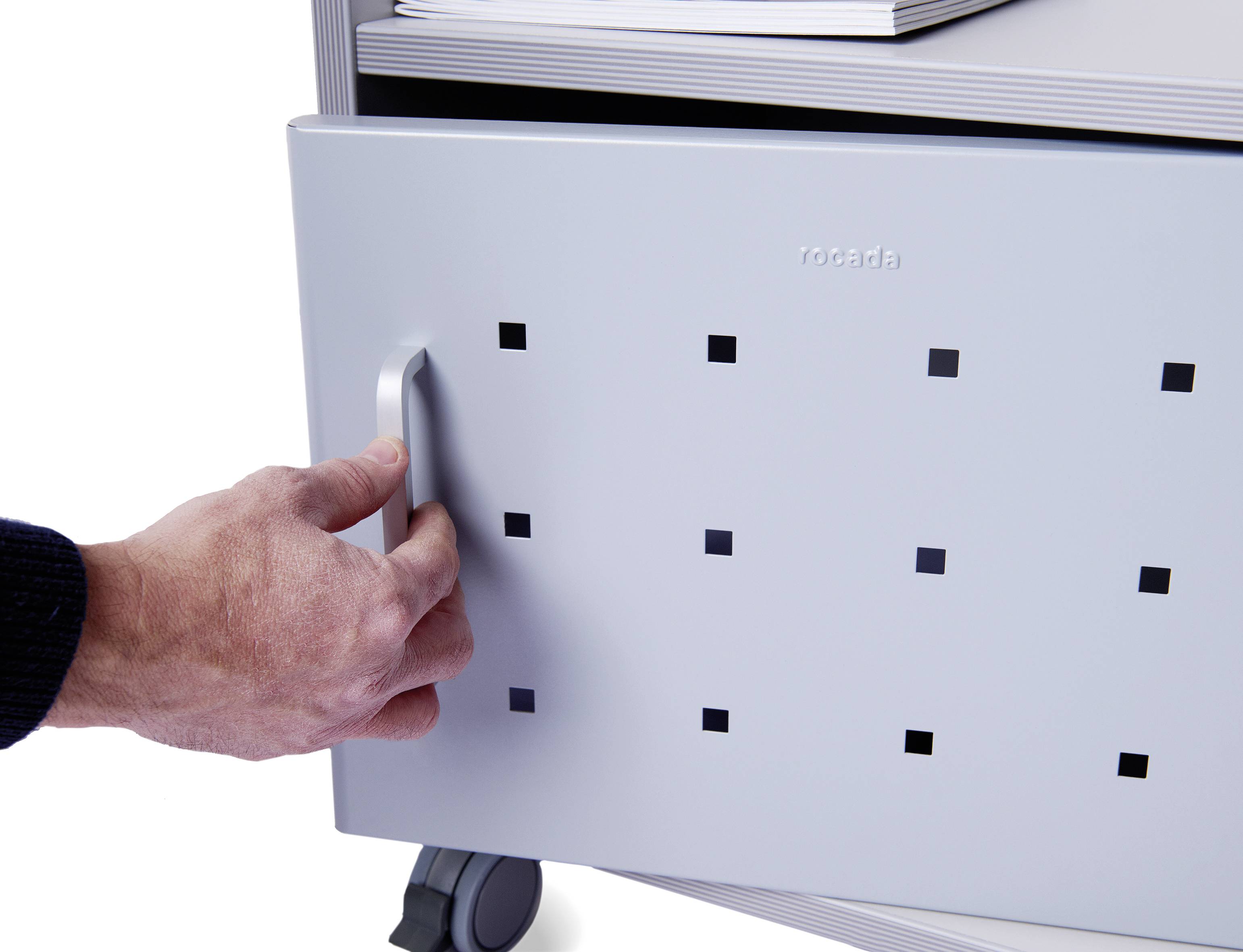 Ręka otwiera szarą szufladę z kwadratowymi otworami w mobilnym systemie meblarskim.