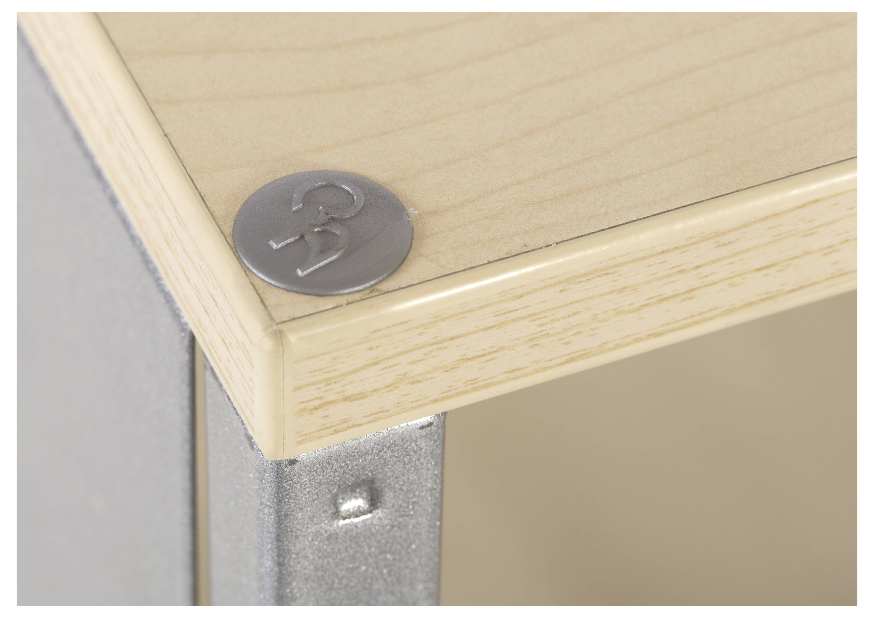 Zbliżenie przedstawia róg drewnianego stołu z okrągłą, srebrną metalową nakładką, na której wygrawerowana jest liczba '33'.