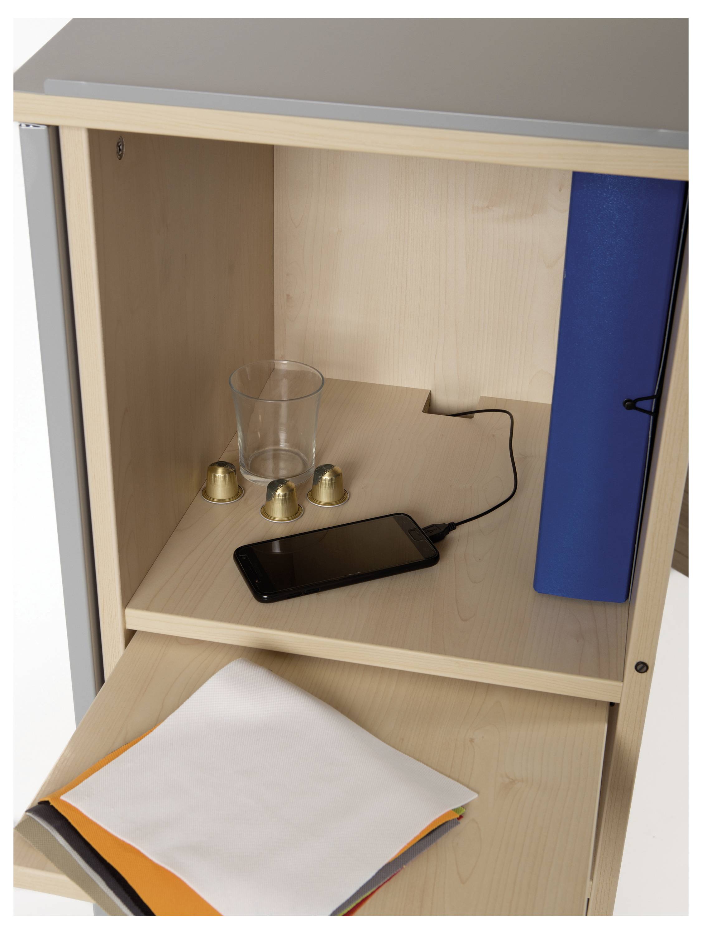 Otwarty drewniany regał z szklanką, trzema małymi metalowymi dzwoneczkami, niebieskim segregatorem i smartfonem ładującym się.