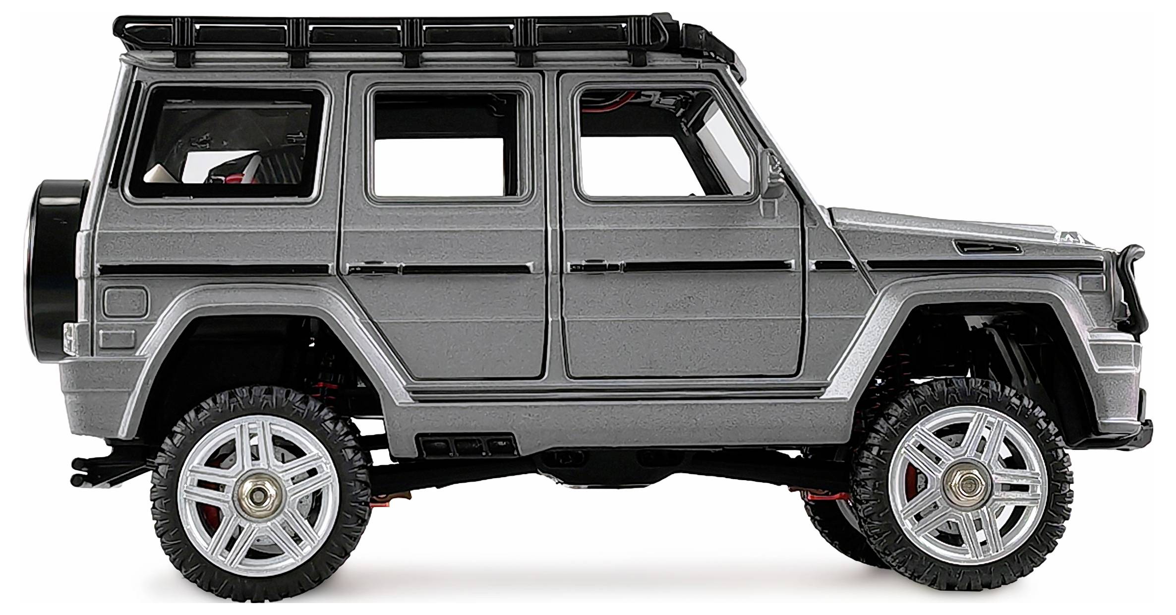 Srebrny samochód terenowy sfotografowany z boku na białym tle, z grubymi oponami i bagażnikiem dachowym.
