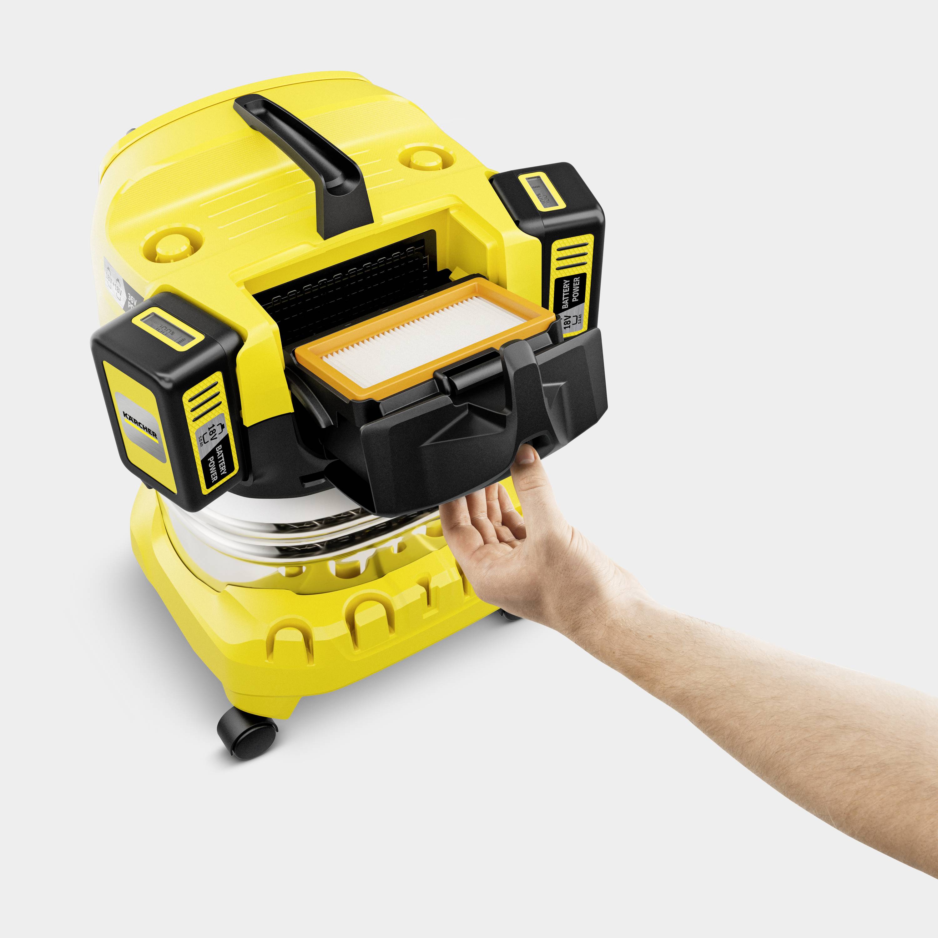 Ręka wskazuje na żółty przemysłowy odkurzacz z otwartą klapką, ukazującą dostęp do filtra.