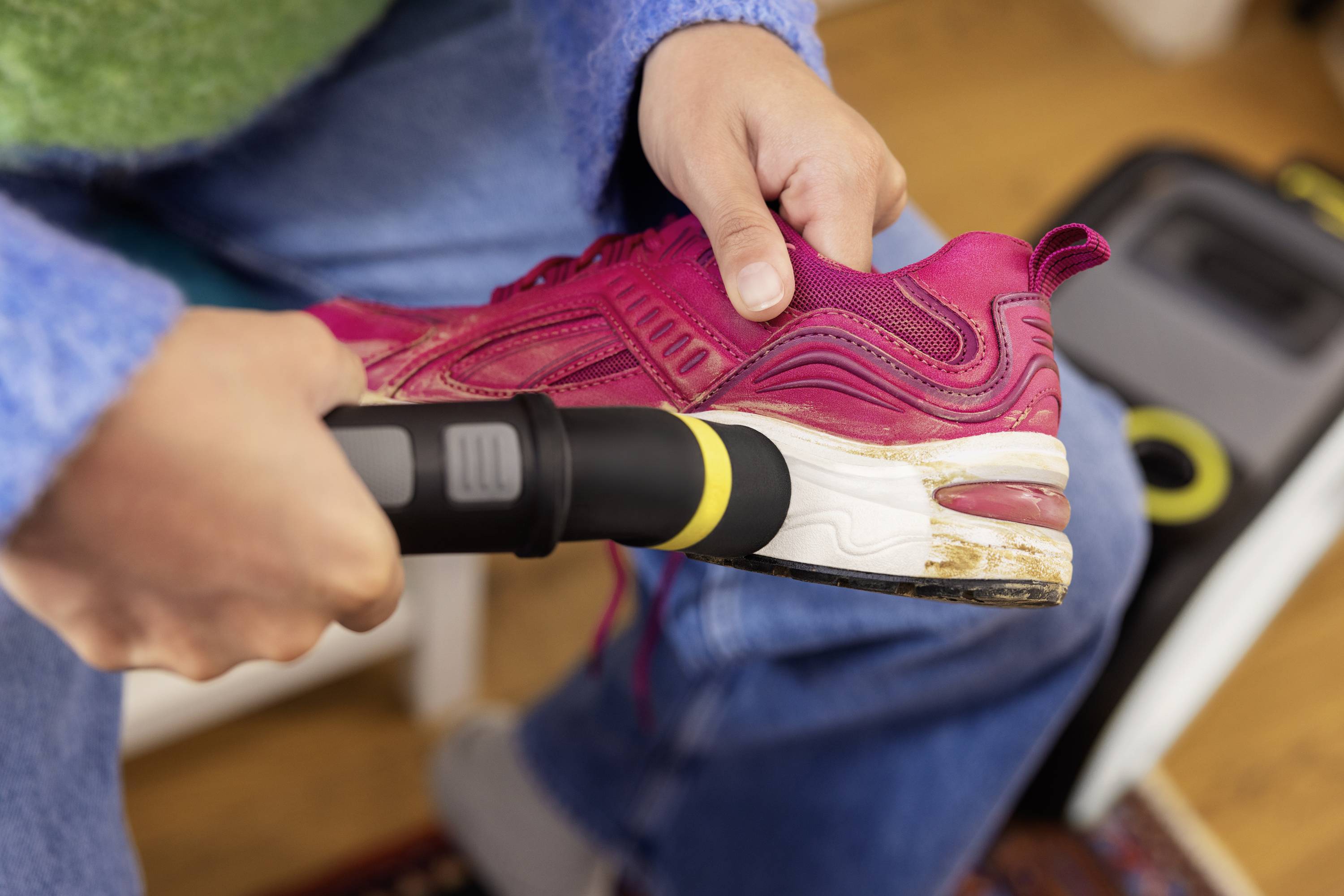 Osoba czyści czerwony but sportowy odkurzaczem. Fokus skierowany jest na podeszwę buta trzymanego w ręku.