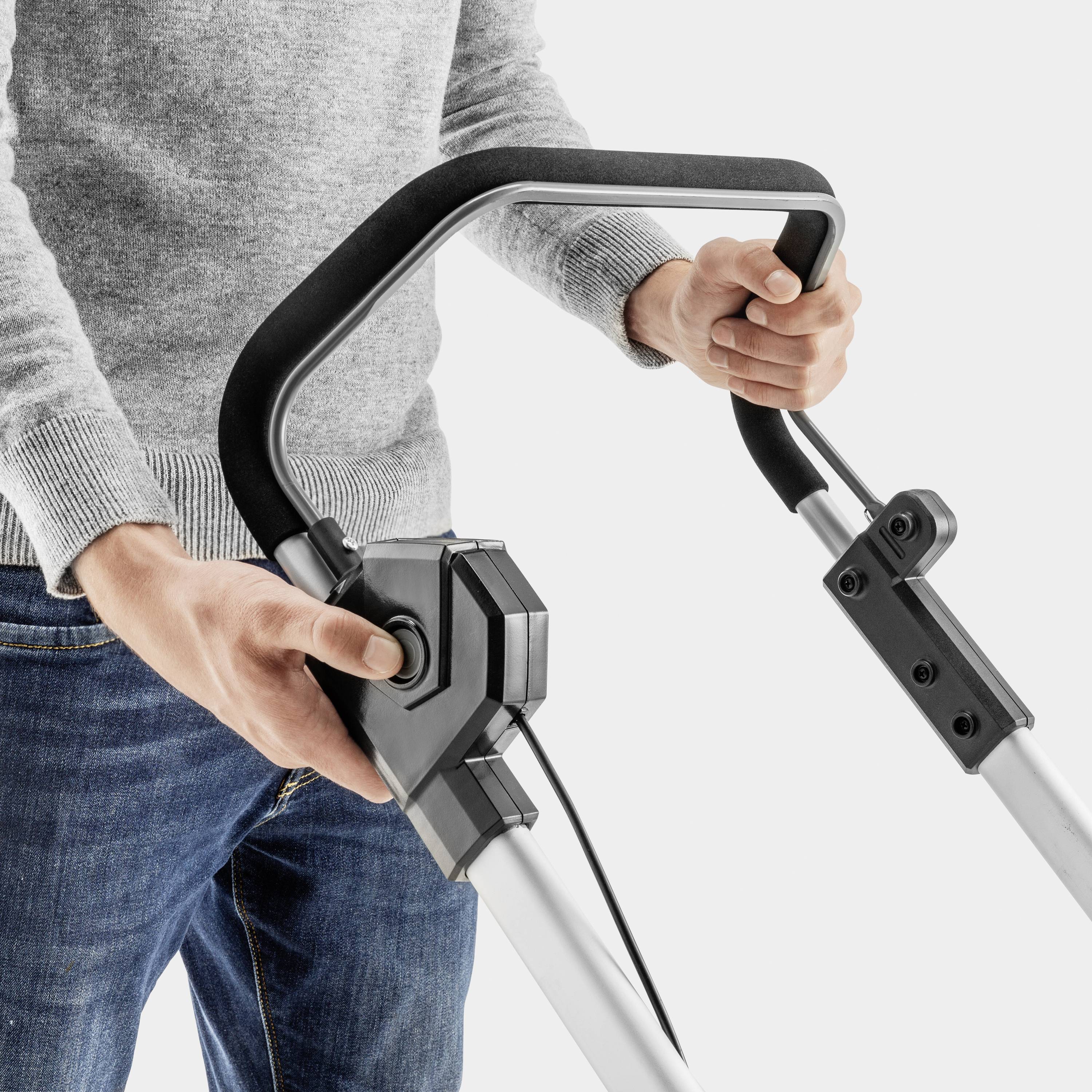 Osoba trzyma uchwyt odkurzacza obiema rękami. Fokus spoczywa na obsłudze urządzenia używanego do czyszczenia podłogi.