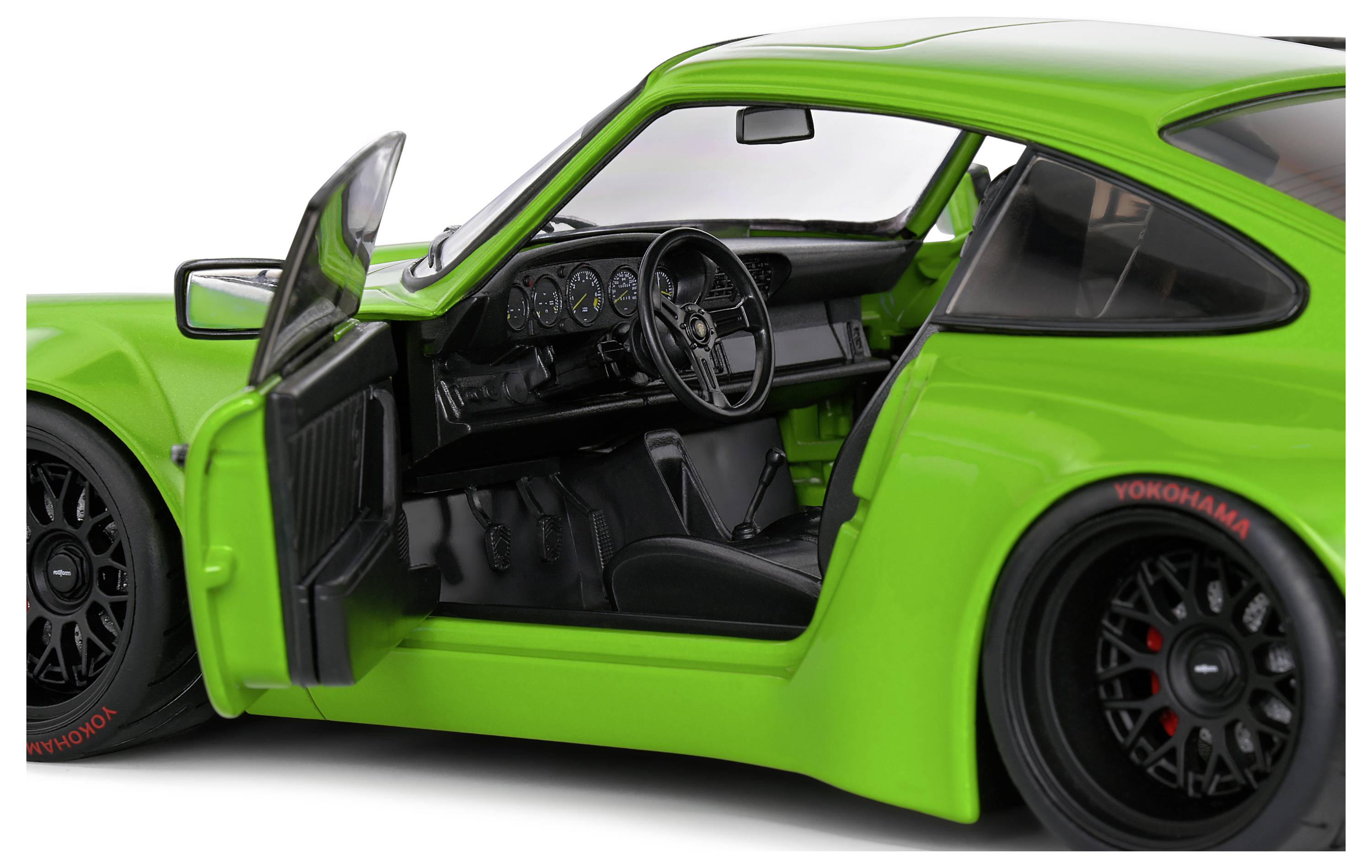 Zielony samochód sportowy z otwartymi drzwiami, prezentujący sportowe wnętrze z kierownicą i deską rozdzielczą. Marka samochodu widoczna na oponach.