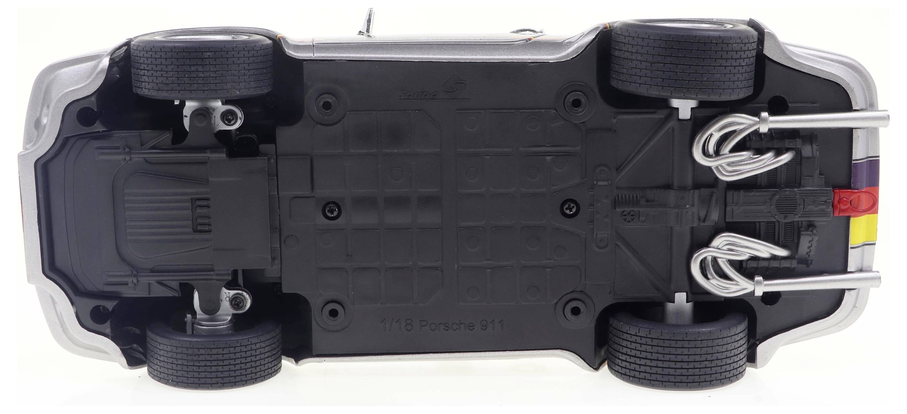 Samochodzik zabawkowy sfotografowany od spodu, ukazujący szczegóły dolnej części, takie jak koła, rury wydechowe i osie.