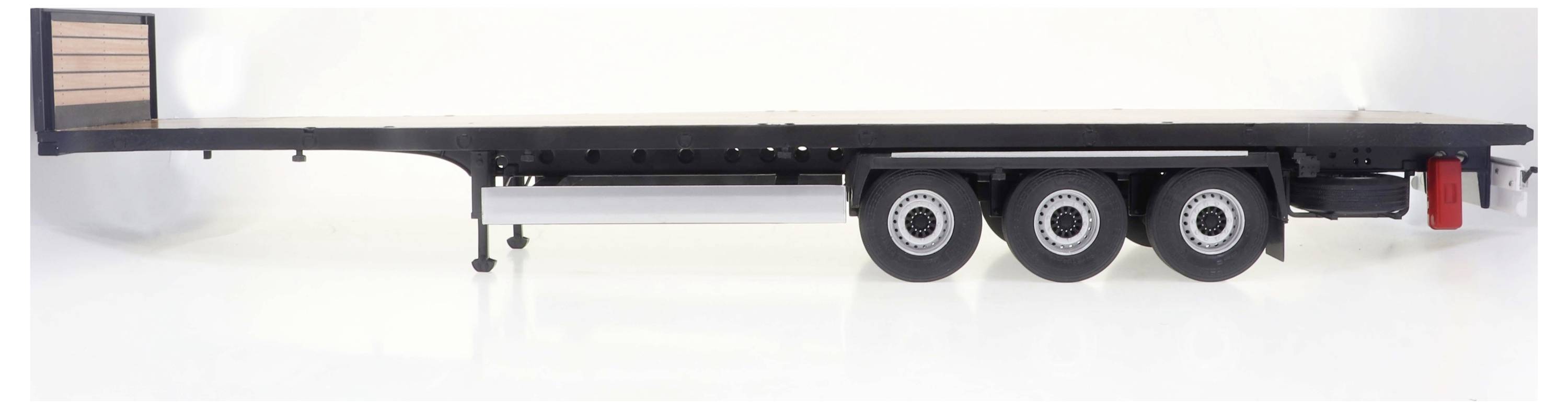 Trzyosiowa platforma transportowa bez ładunku. Widok z boku ukazuje koła i ramę platformy na białym tle.