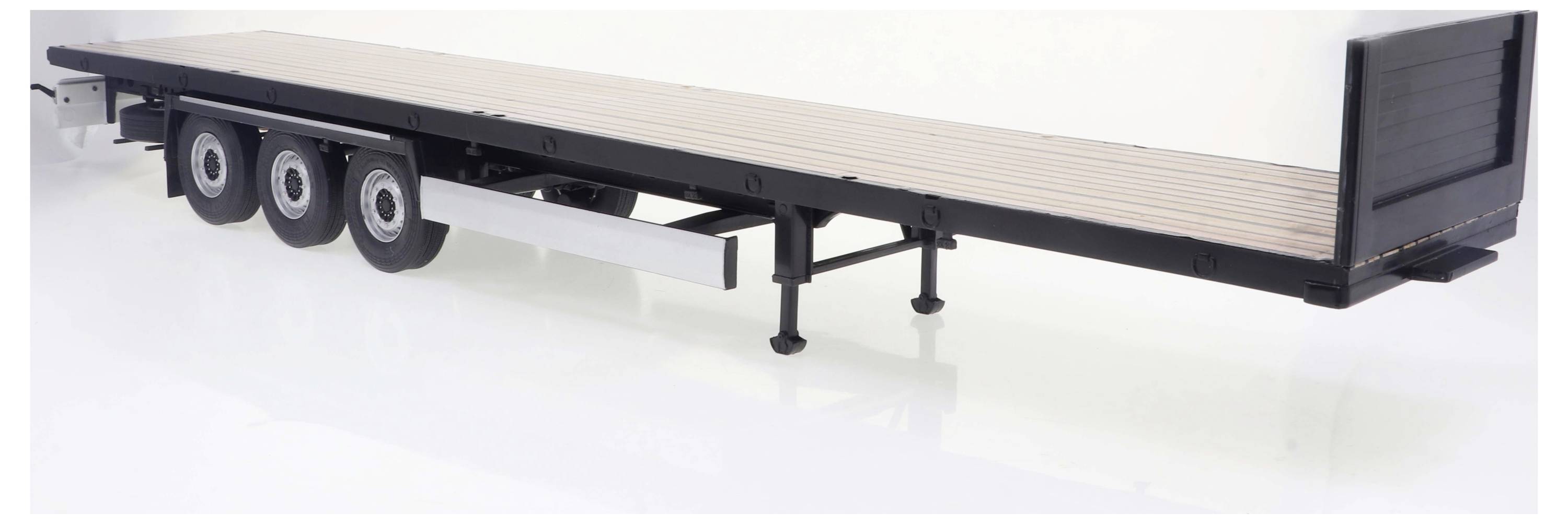 Długa, płaska przyczepa z trzema osiami i drewnianymi deskami na powierzchni ładunkowej, podparta metalowymi nogami, stoi na białym tle.