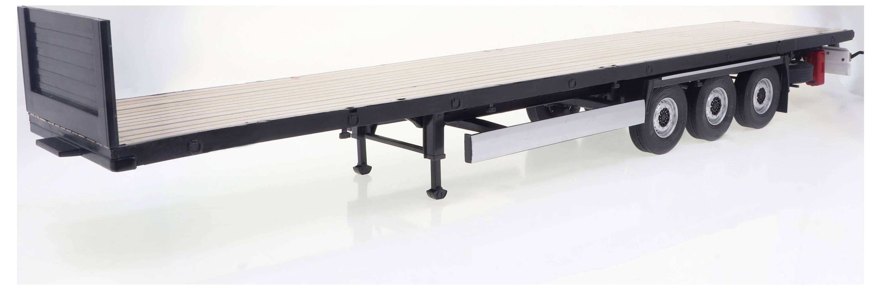 Długa, płaska przyczepa z trzema osiami, wykonana z metalu i drewna, stoi na powierzchni wystawowej.
